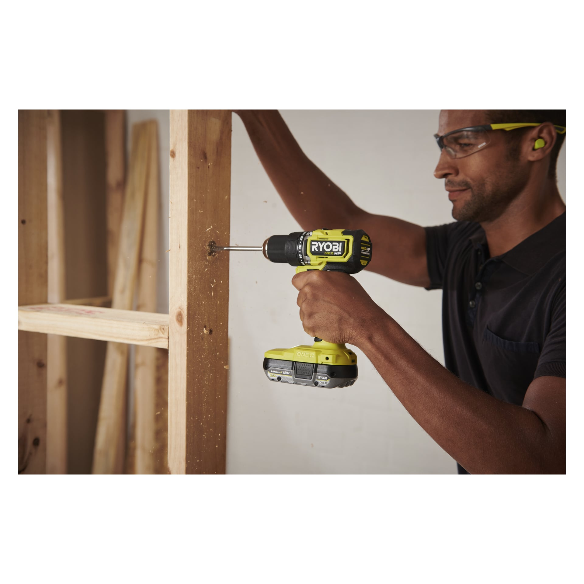 En person med skyddsglasögon borrar in i en vertikal träbalk med en Ryobi One+ HP borstlös borrmaskin, mitt i stomarbete.