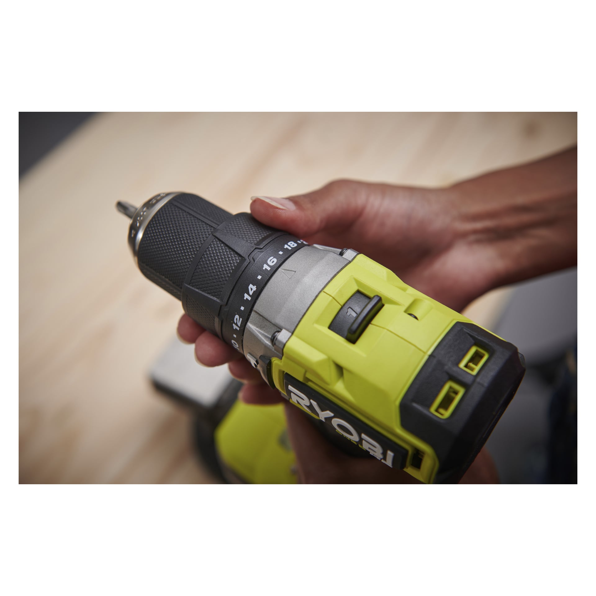 Man justerar vridmomentet på en gul och svart Ryobi One+ HP borstlös skruvmejsel. En suddig ljus träyta är bakom.