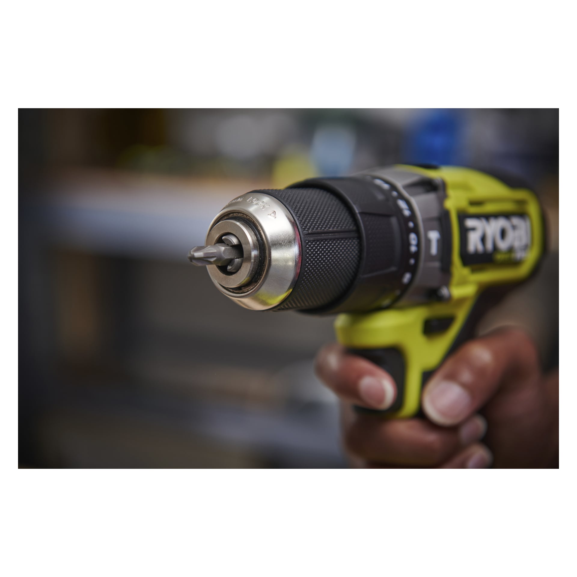 Handgrepp om en Ryobi One+ HP Brushless slagverksskruvmejsel RPD18C1-0 med en bit i chucken, bakgrunden mjukt suddig.
