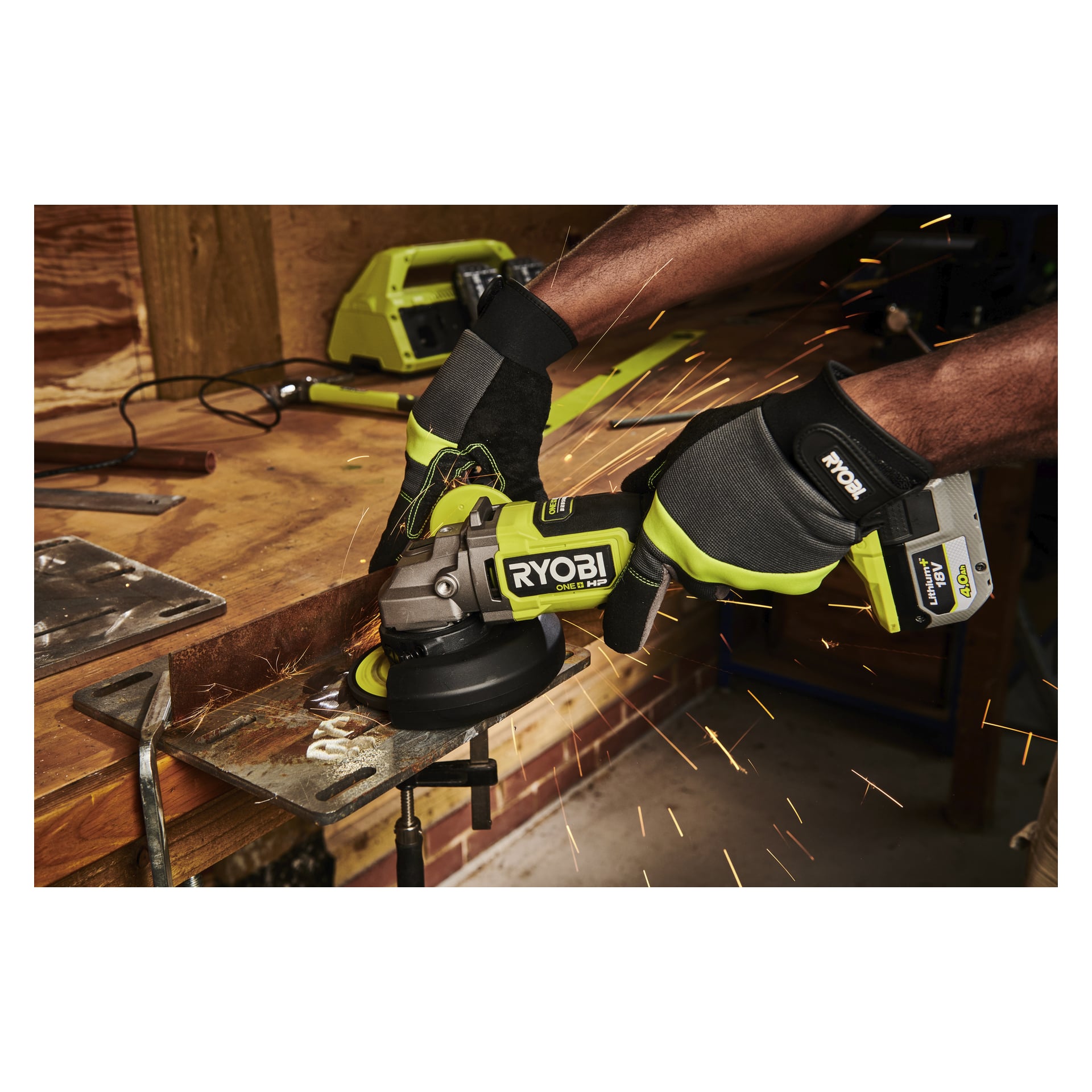 Hansikoitu henkilö hioo metallikappaletta Ryobi One+ HP -kulmahiomakoneella, jolloin kipinöitä syntyy työpöydällä työpajassa.