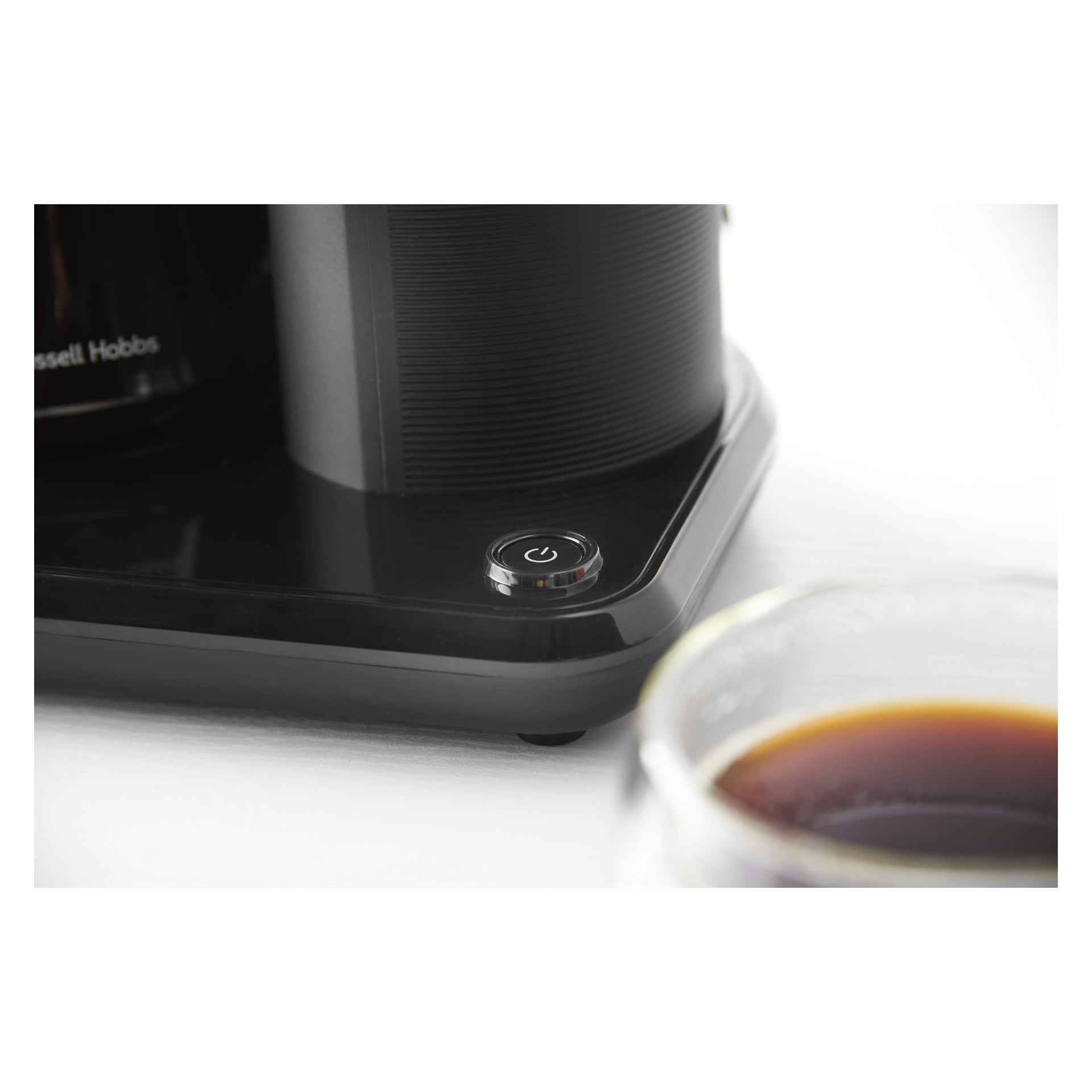 Närbild på strömknappen på Russell Hobbs Attentiv Black kaffebryggare, med en glaskopp svart kaffe i förgrunden.