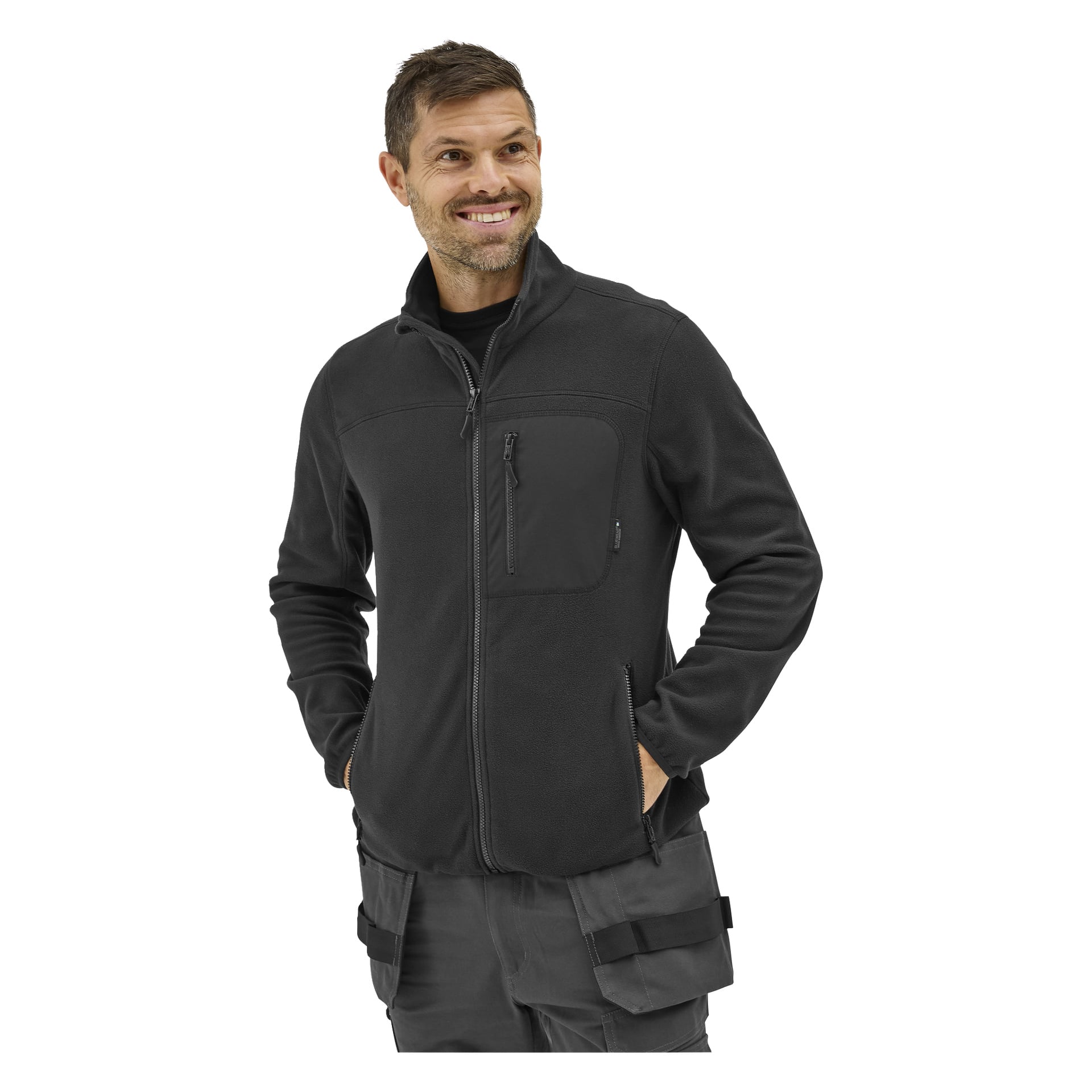 Man ler i en "Bluewear Men's fleece jumper Filip" med svart bröstficka, klädd i mörkgrå cargobyxor. Hans händer är i fickorna och han tittar åt sidan.