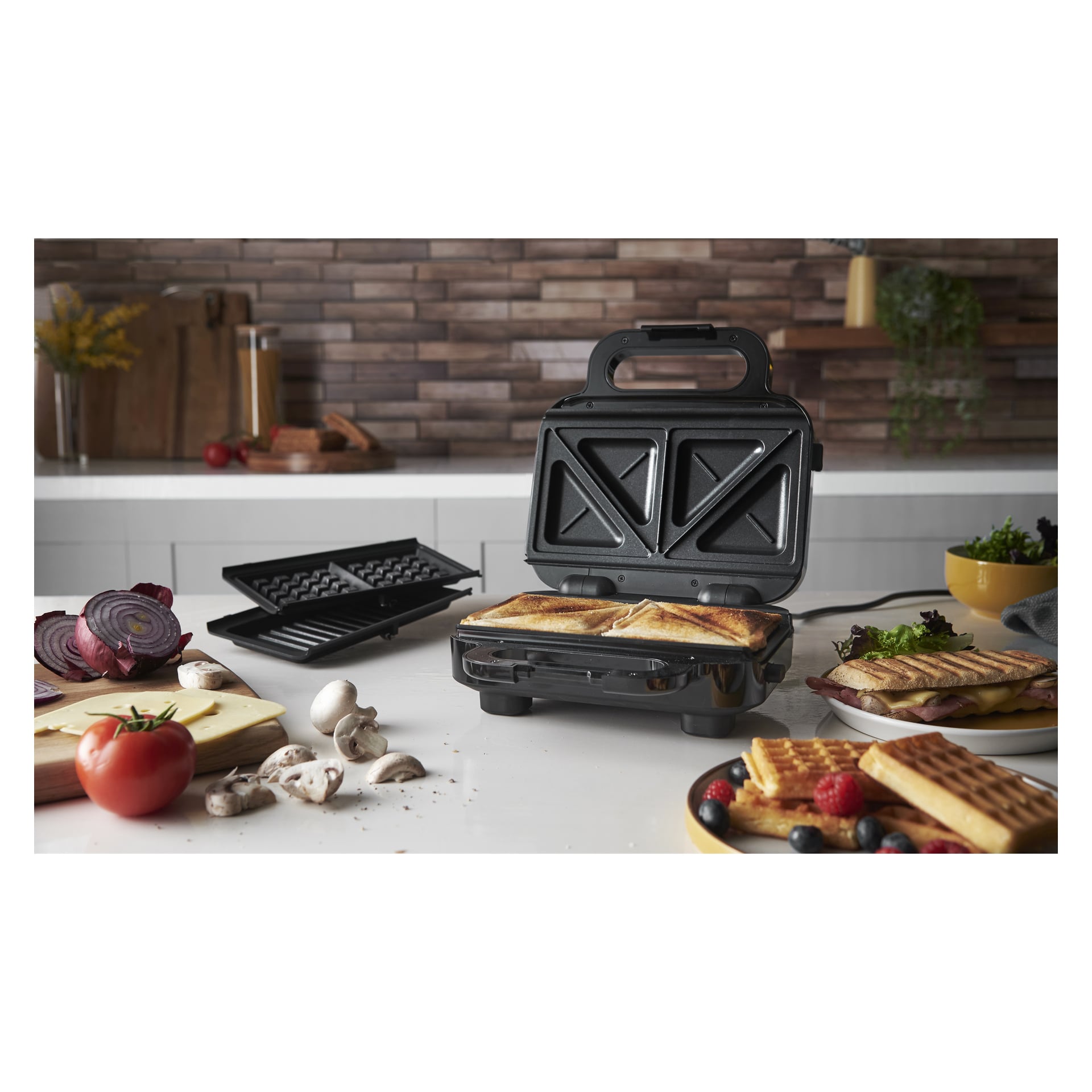 Russell Hobbs Sandwich grillaa 3-in-1 keittiötasolla, tehden kolmiomaisia voileipiä. Lähellä: vihanneksia, juustoa, vohveleita marjoilla, ylimääräisiä lautasia.