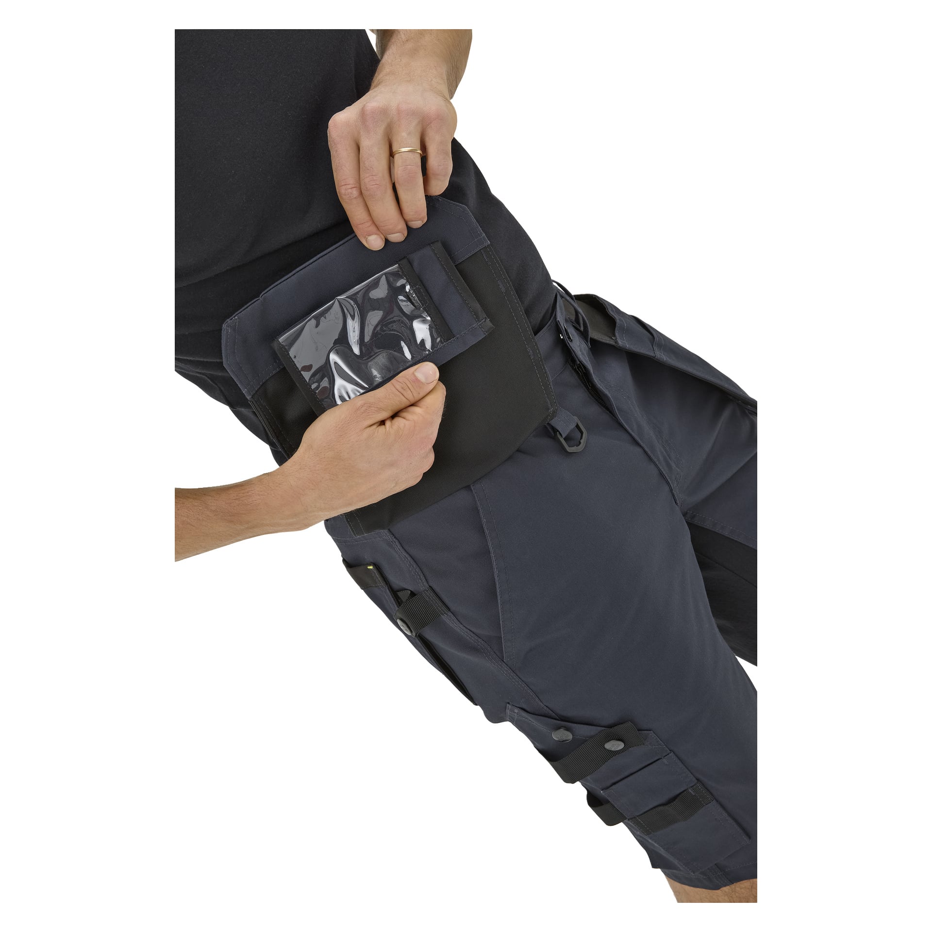 En person i Bluewear Men's Rex arbeidsshorts løfter lårlommen og avslører en klar del for ID; iført svart skjorte og ring.