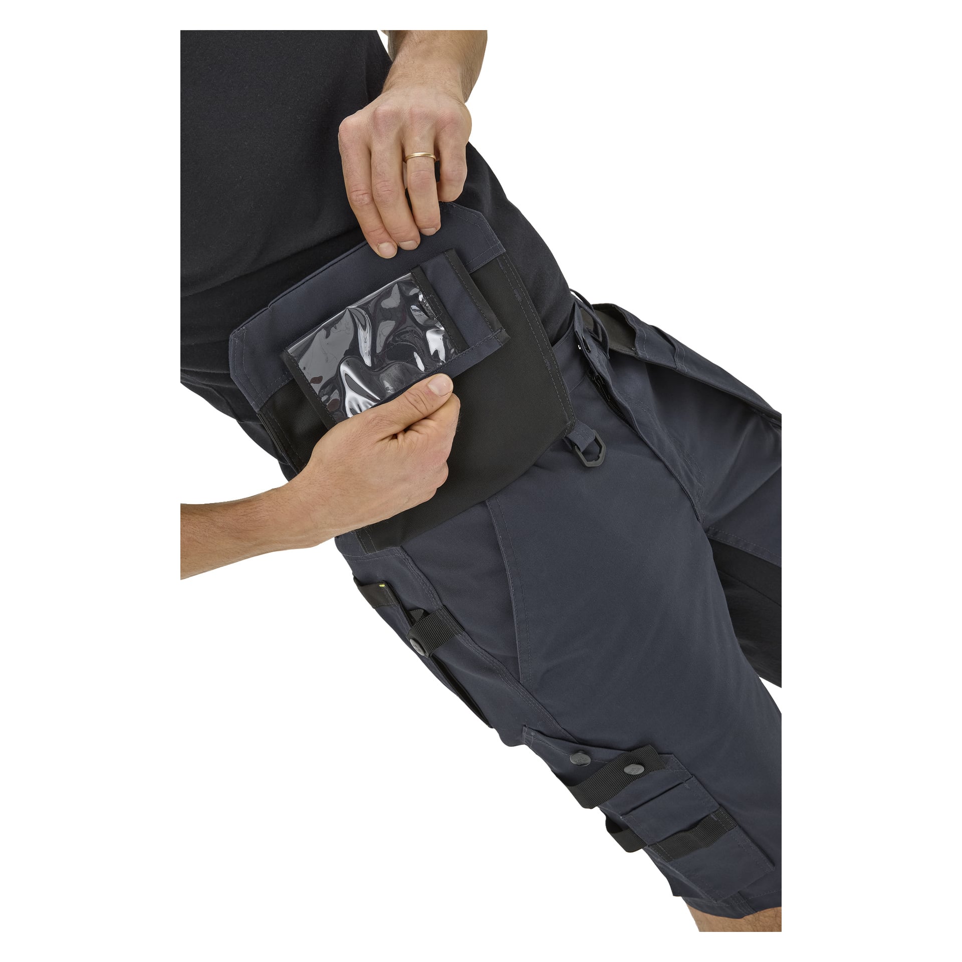En person i mörkblå Bluewear Men's Rex arbetsshorts med svarta detaljer lyfter en flik för att visa en transparent lårficka; bål och lår visas.