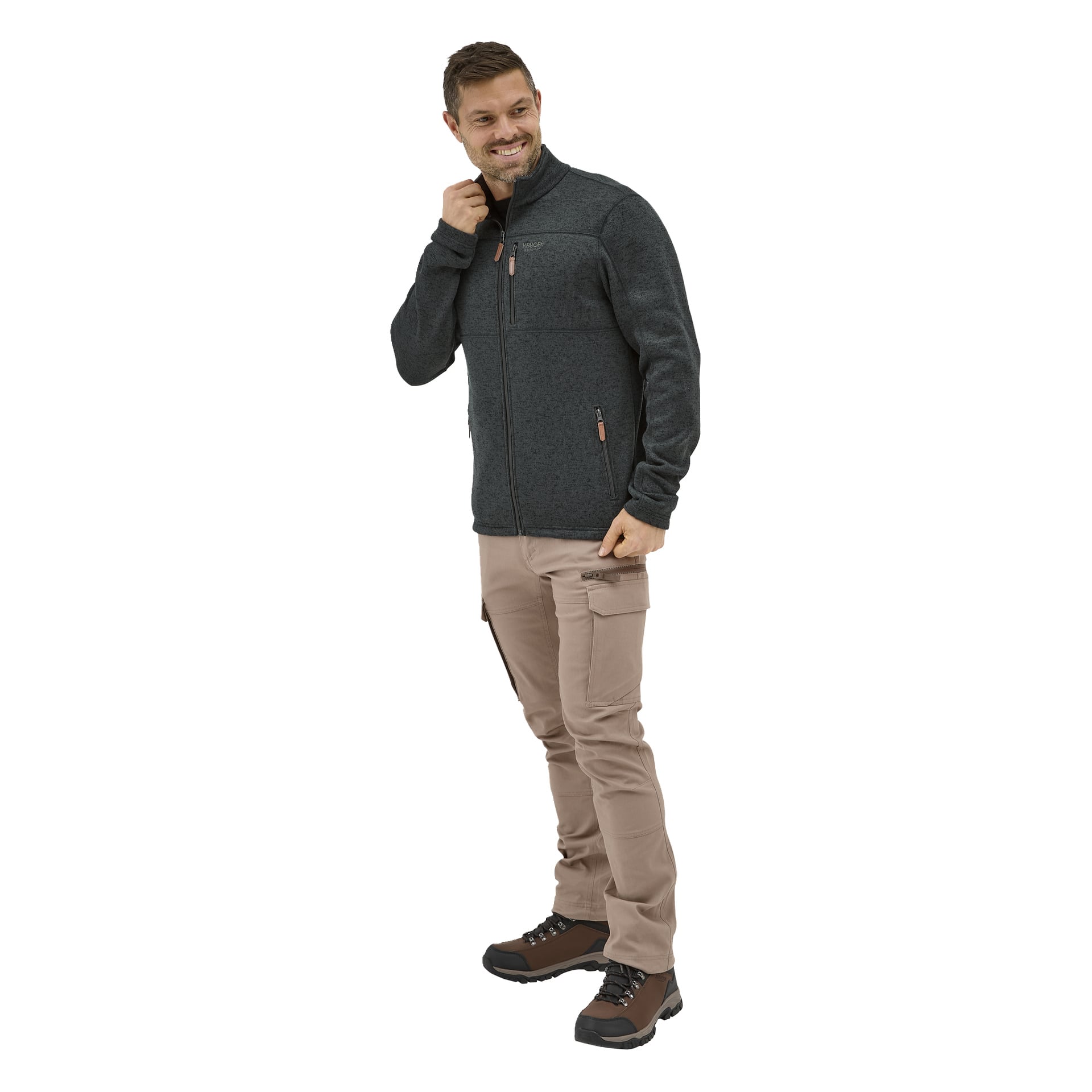 Ein lächelnder Mann trägt beige Kayoba Outdoor Herrenhosen von Åsen, eine dunkle Fleece-Reißverschlusshose und braune Wanderschuhe, die seinen Jackenkragen halten.