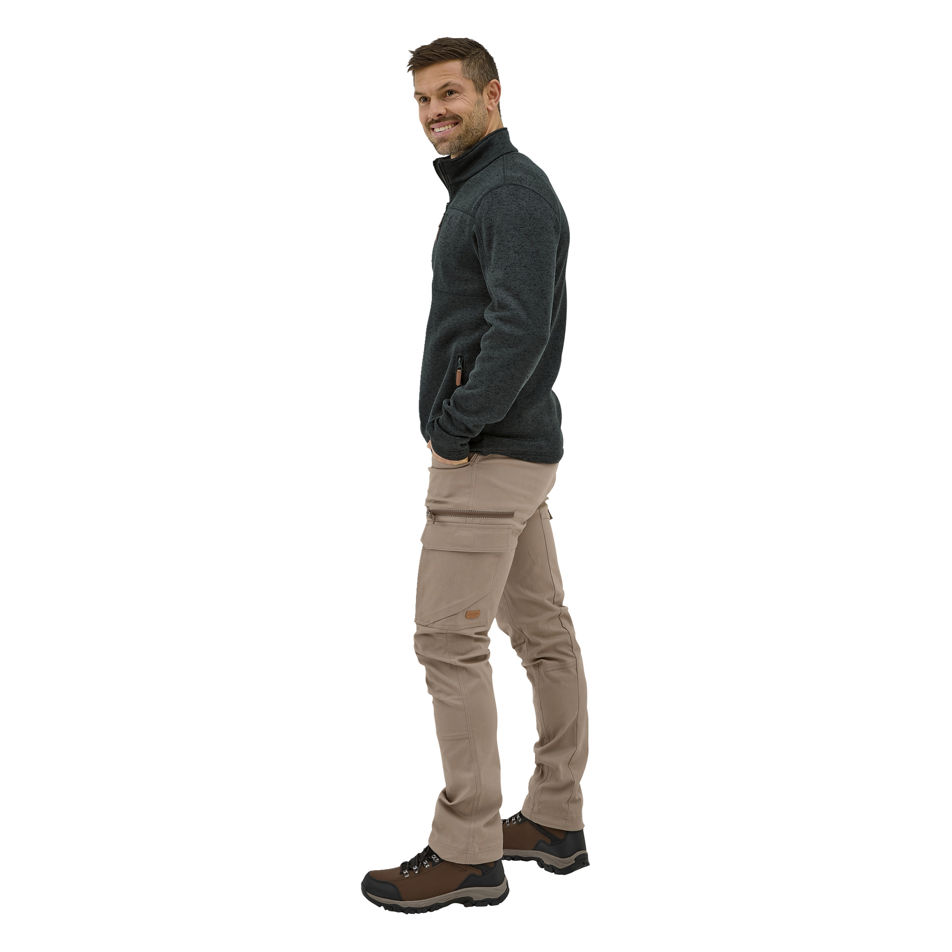 Ein lächelnder Mann steht seitlich mit der linken Hand in der Tasche, trägt eine Outdoor-Hose von Åsen und eine dunkle Reißverschlussjacke und blickt nach rechts.