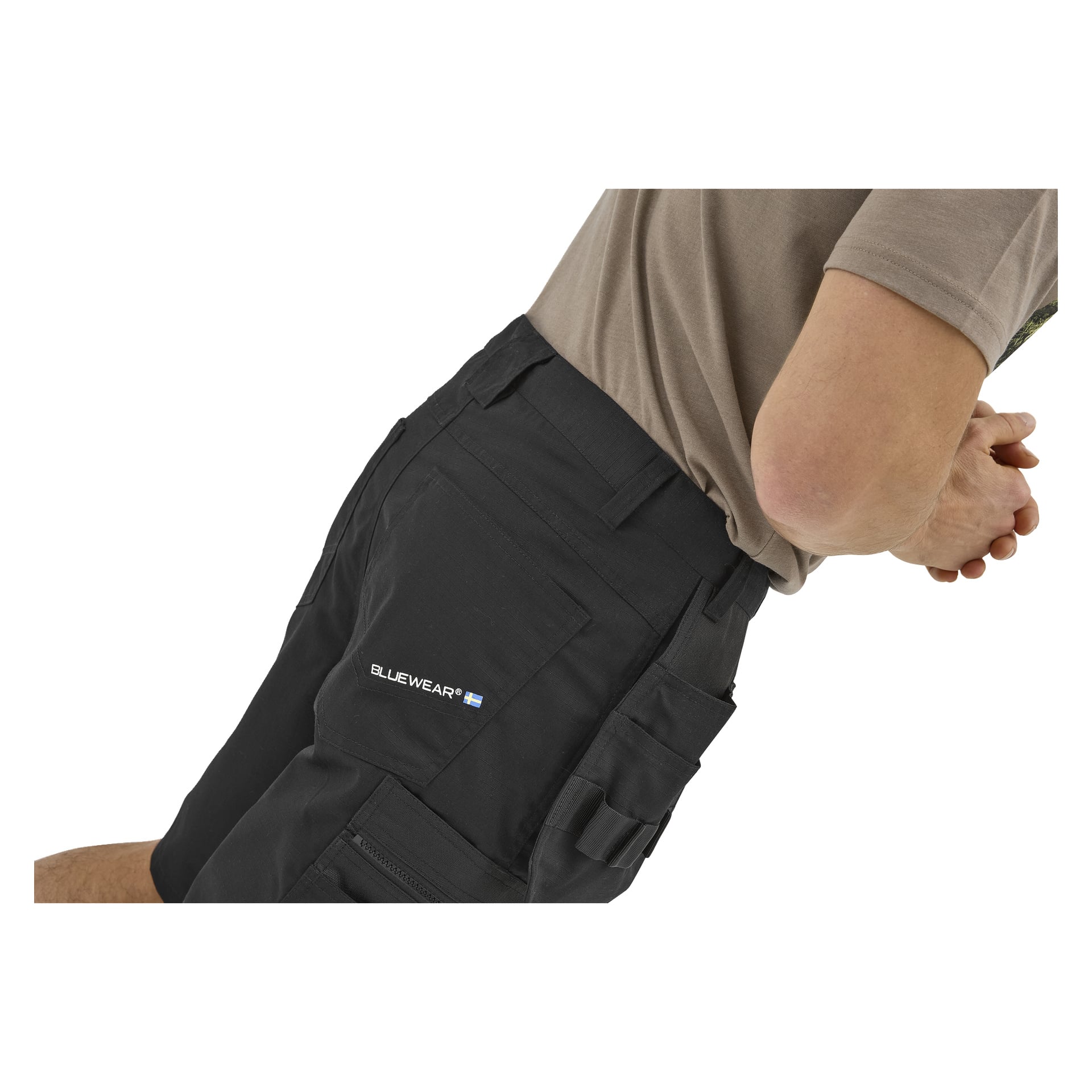 En person lutar sig fram med händerna knäppta, klädd i en taupefärgad skjorta och svarta Bluewear Men's work shorts; ben och överkropp visade.
