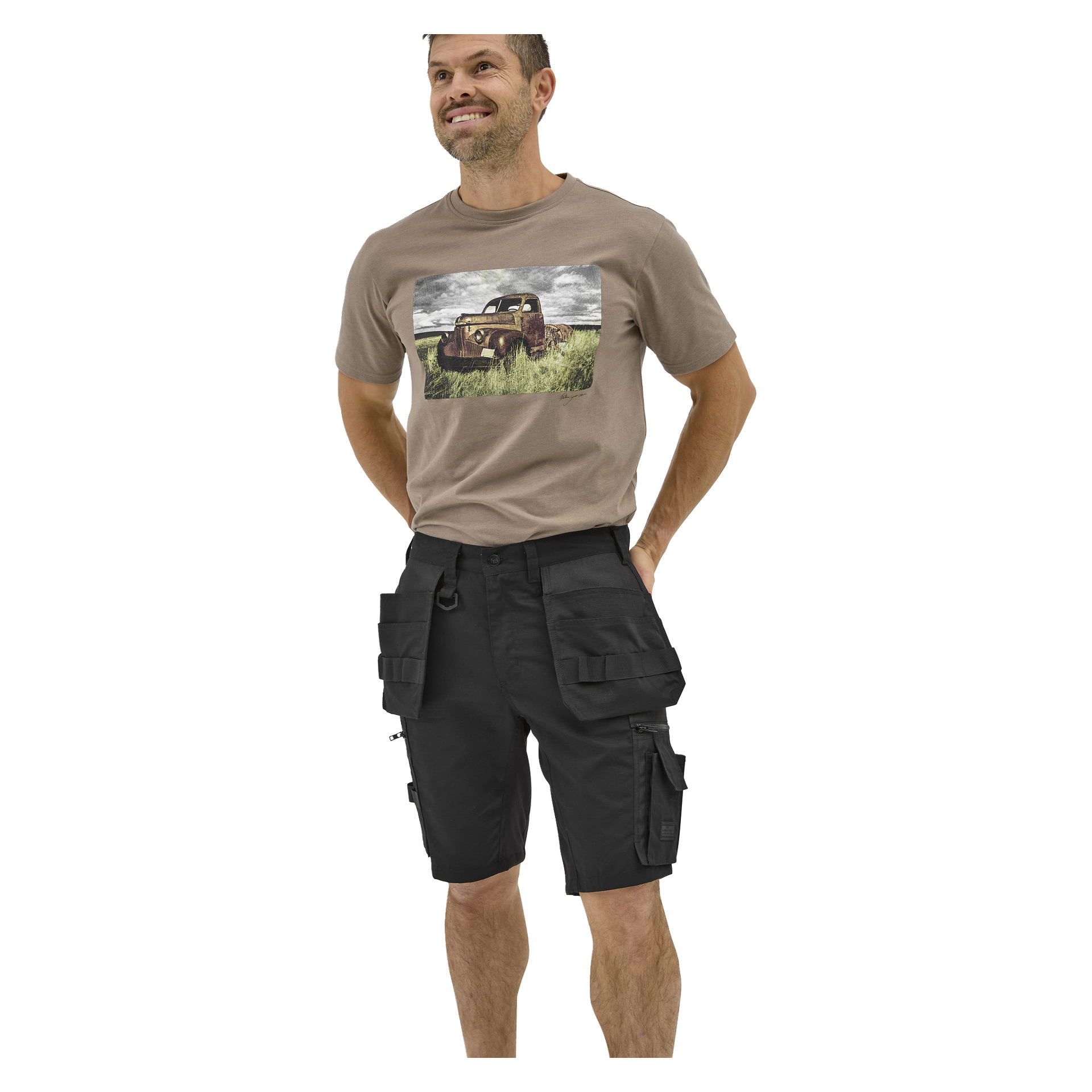 En leende man bär en beige t-shirt med gammal lastbilsgrafik och svarta Bluewear Men's Micke work shorts med flera fickor.