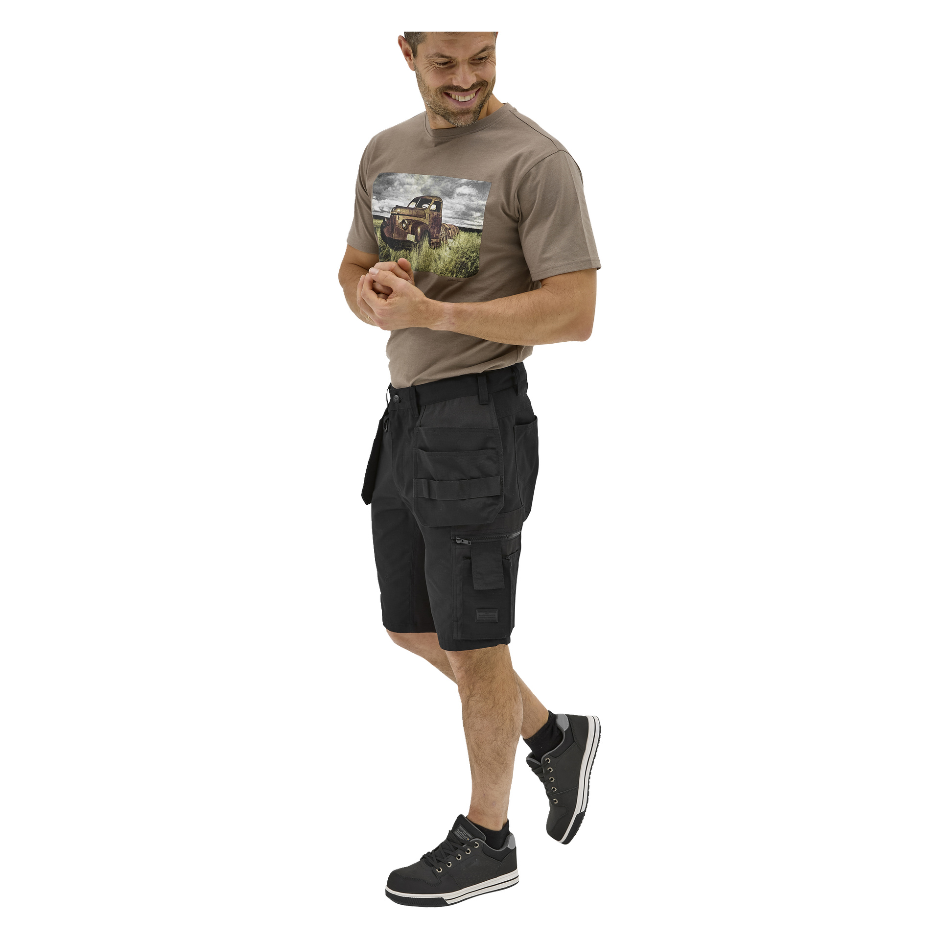 En leende man bär en brun grafisk t-shirt med bildesign, svarta Bluewear-arbetsshorts med fickor och svarta sneakers med vita sulor.