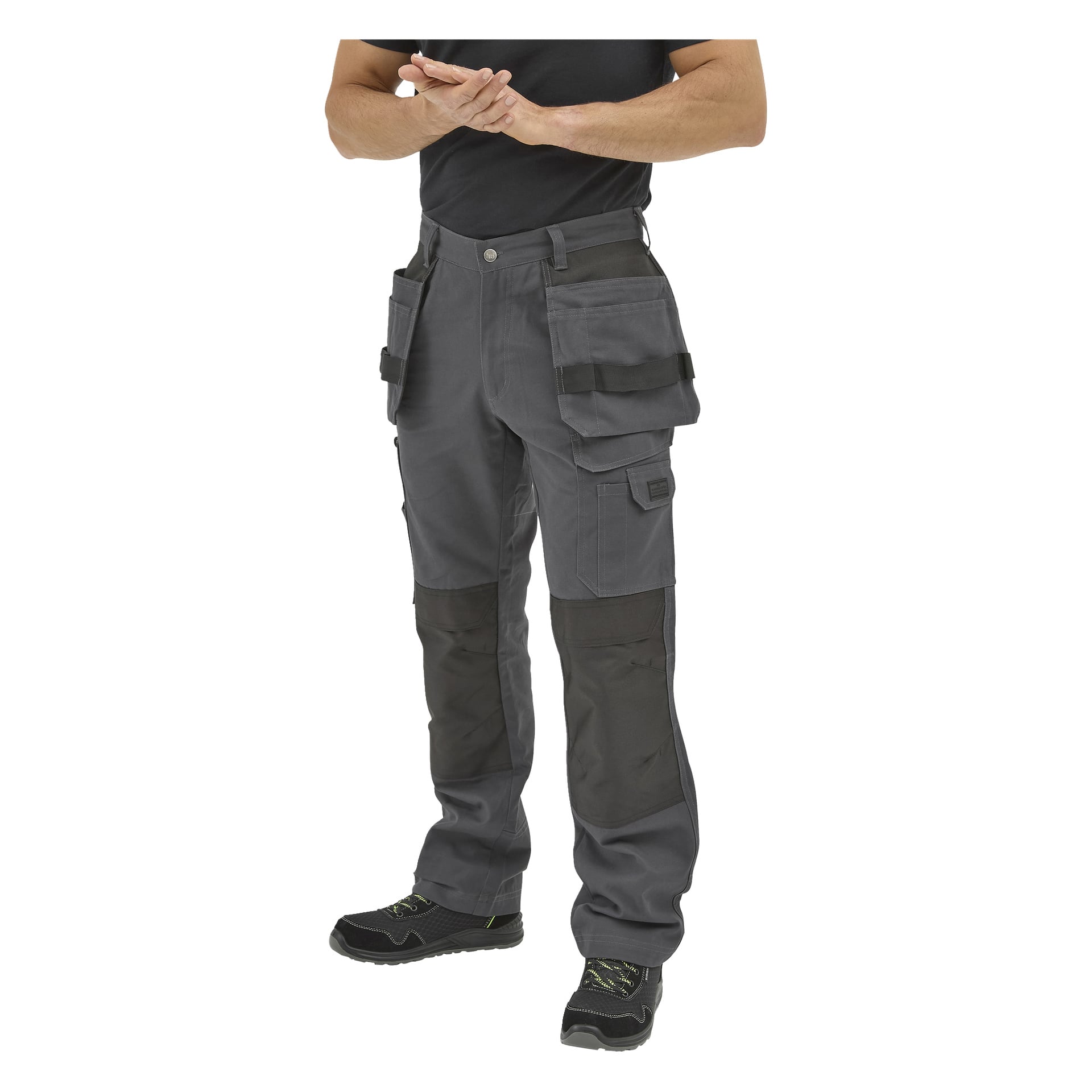 Person klädd i Bluewear Work-byxor med fickor och förstärkta knän, svart t-shirt och arbetsskor, stående händer knäppta.