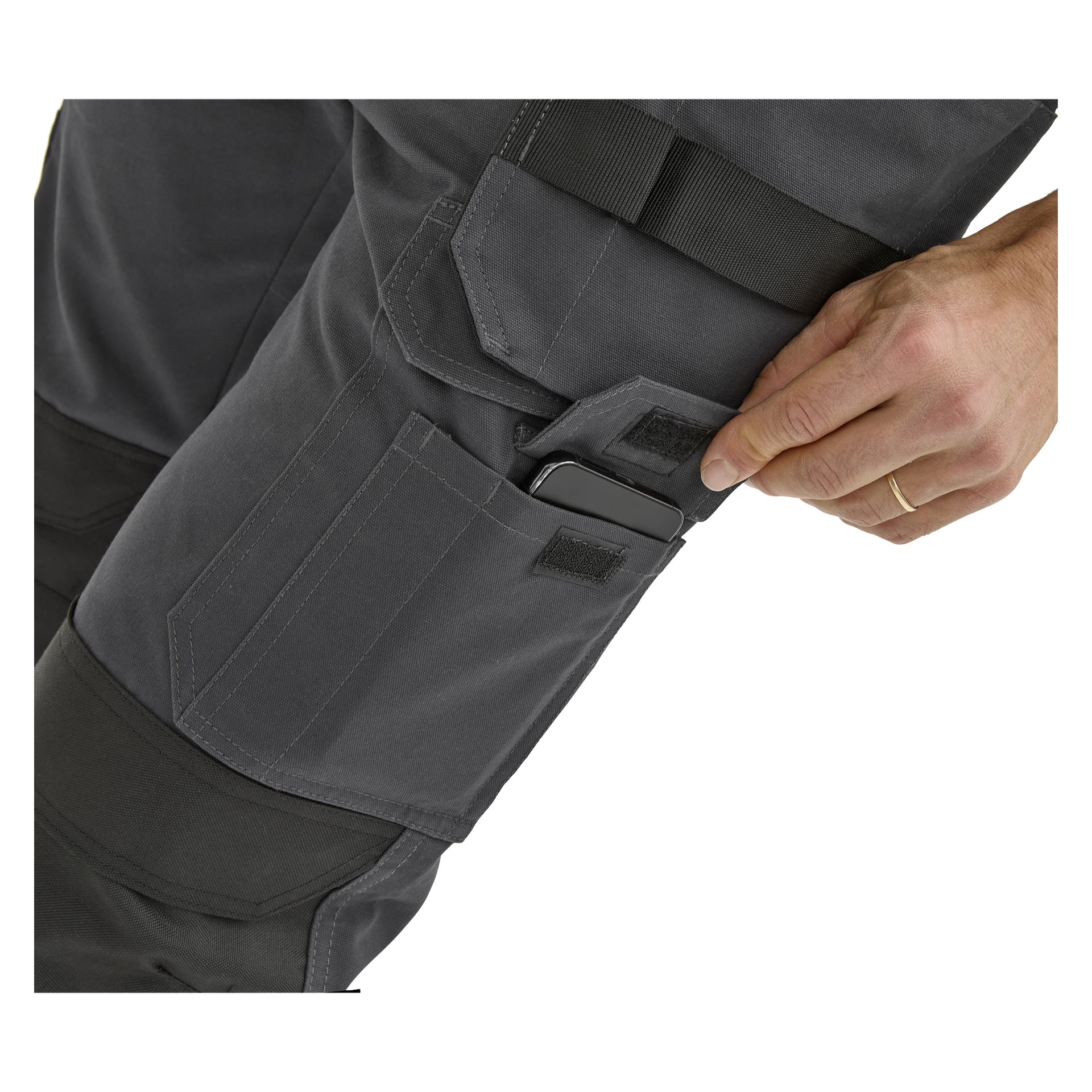 En hand stoppar en smartphone i sidofickan på mörkgrå Bluewear Work Trousers med förstärkta fickor; Byxor och hand visades bara.