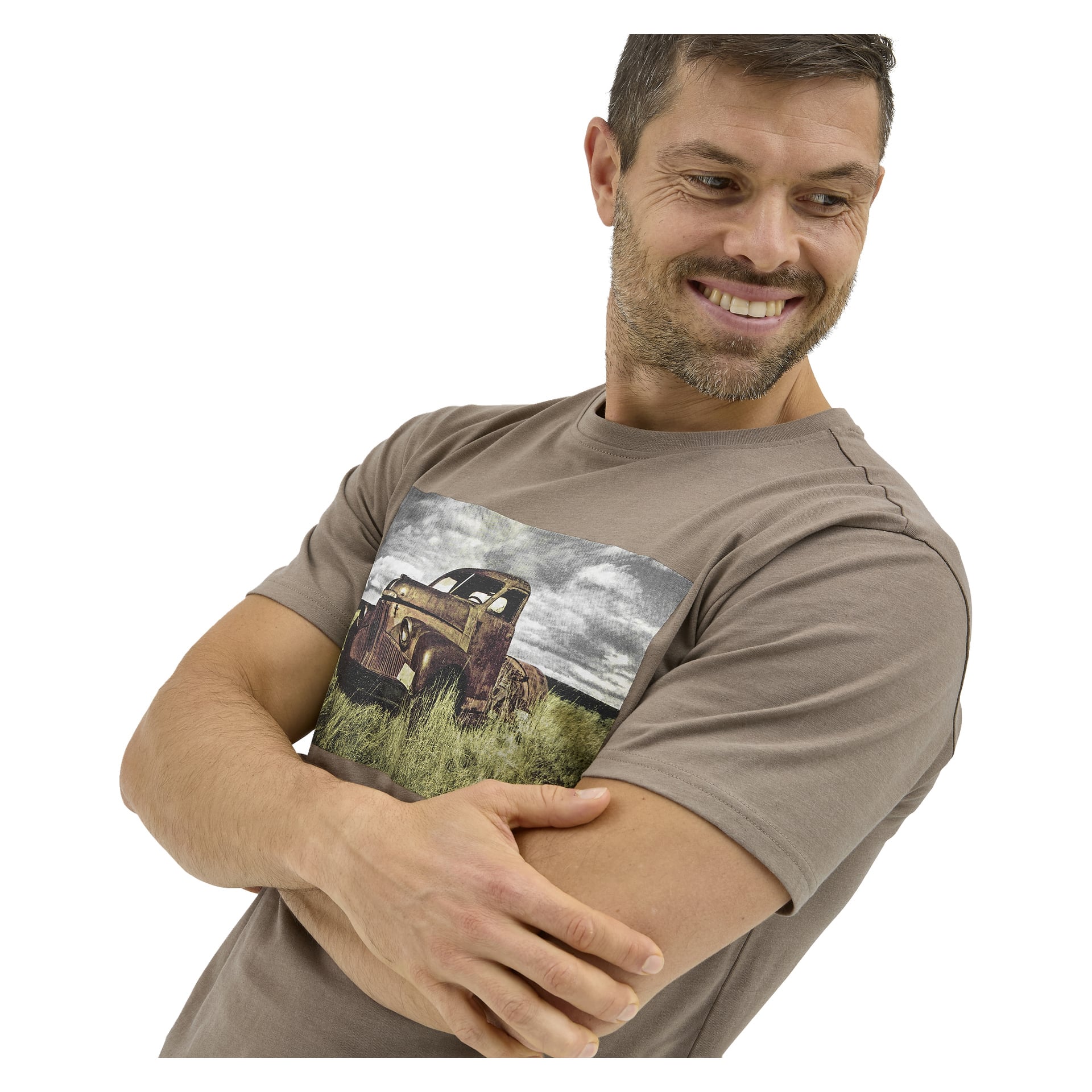 En leende man med kort hår och skägg korsar armarna, iklädd en Bluewear-T-shirt med en gammal lastbil på en gräsmatta.