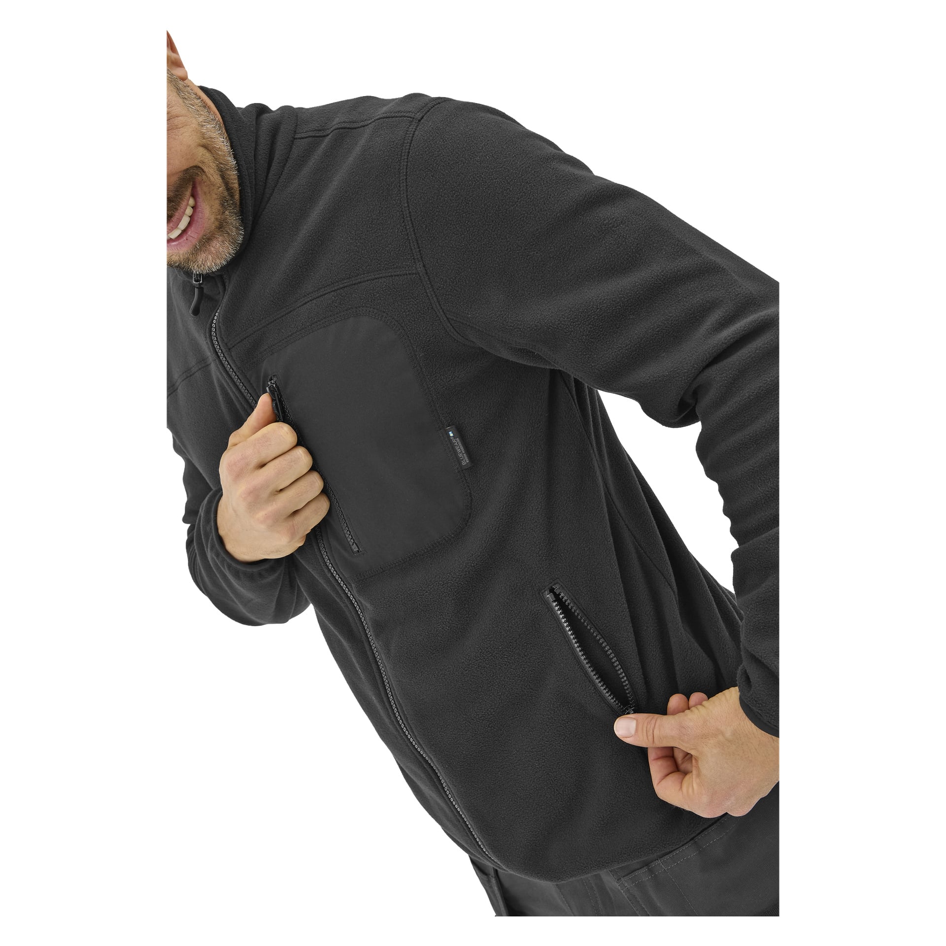 En person som bär en herrfleece-tröja Filip från Bluewear drar dragkedjan på en sidoficka med ena handen, medan den andra handen är nära en bröstficka.