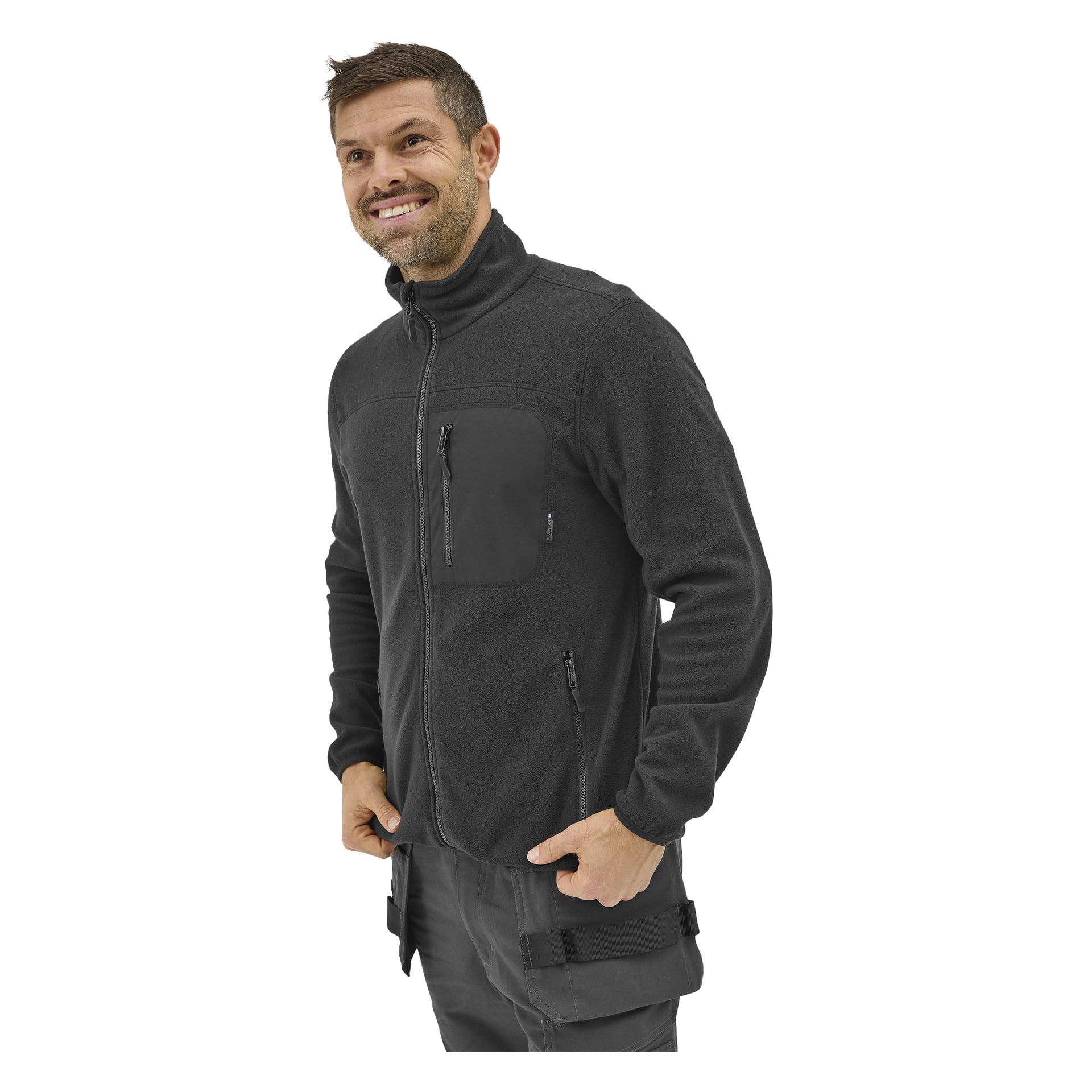 En man med kort hår och skägg ler, klädd i "Bluewear Men's fleece jumper Filip" och grå byxor.