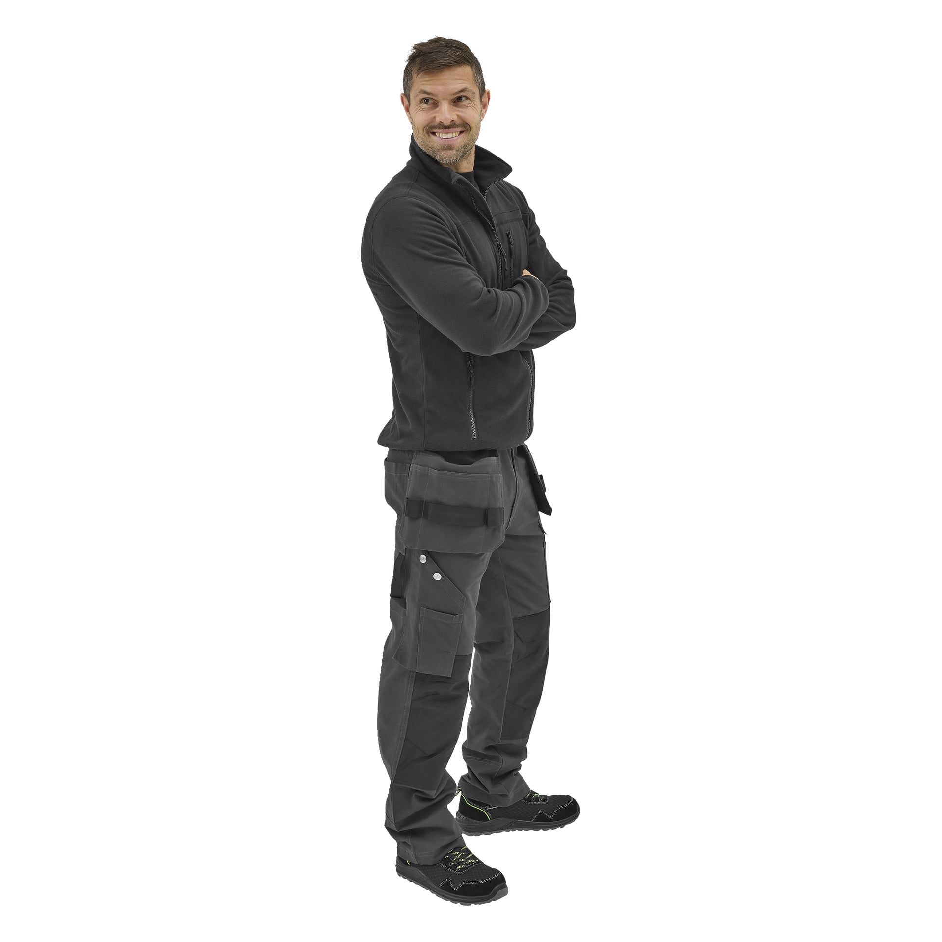 En person står med armarna i kors, klädd i herrfleecetröjan Filip från Bluewear, mörka cargobyxor och svarta sneakers med gula detaljer, tittar lite åt sidan och ler.
