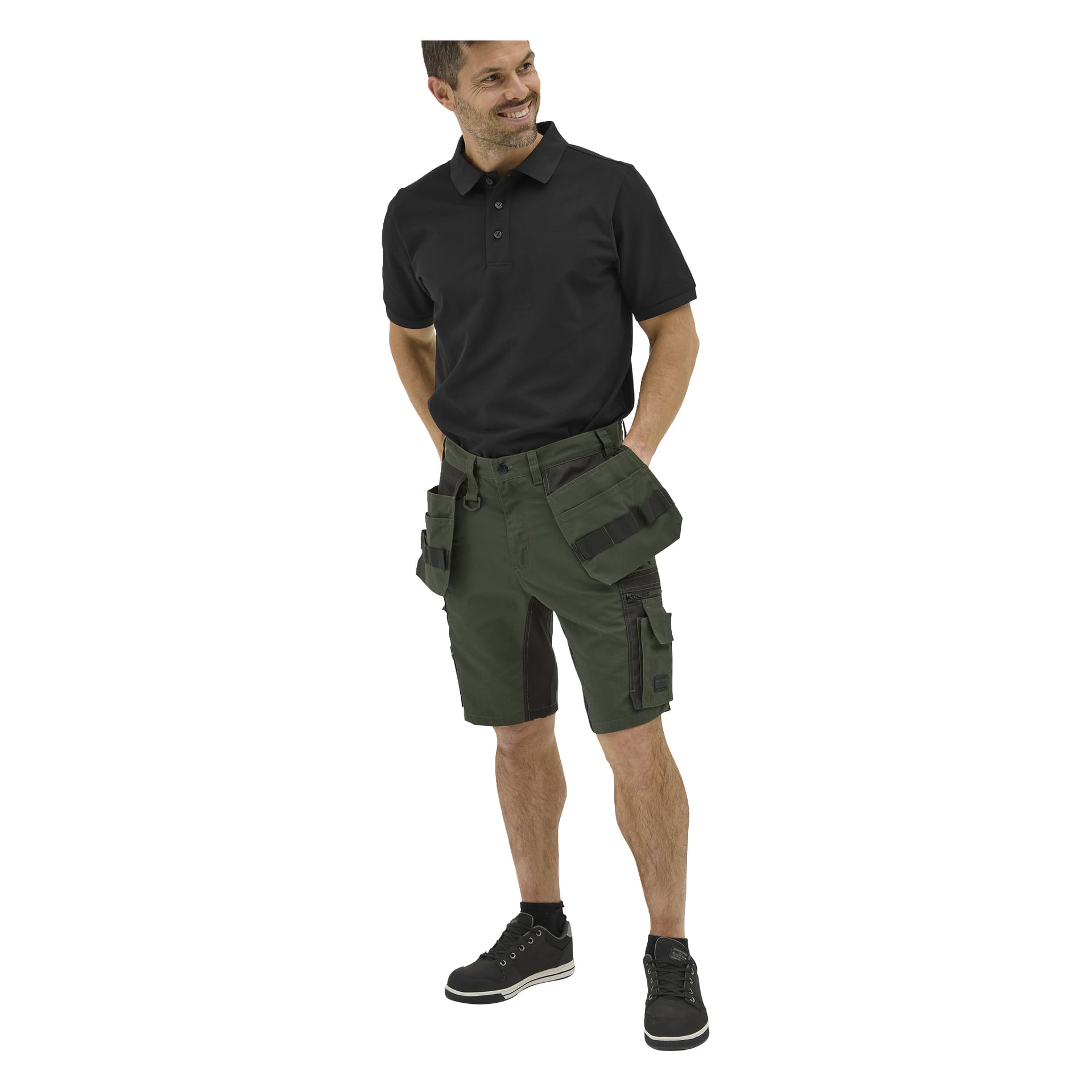 Leende man i en kortärmad svart Bluewear-pikétröja, gröna arbetsshorts med fickor och svarta sneakers med vita sulor.