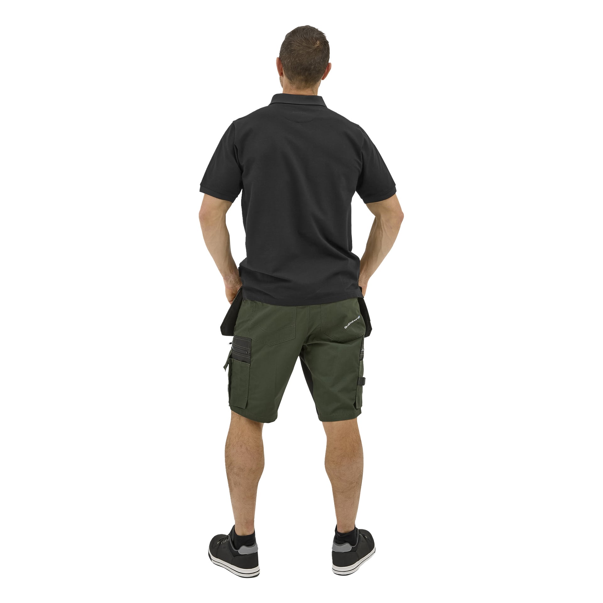 En man står vänd bort, klädd i en Bluewear Putte-pikétröja, gröna cargoshorts och svarta sneakers med händerna i fickorna.