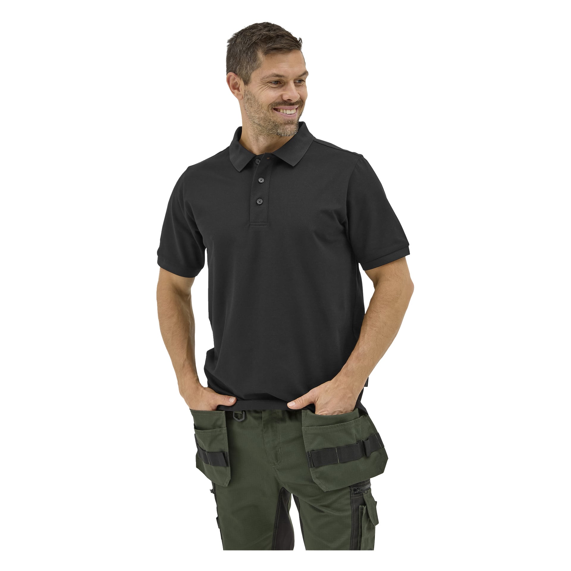 En man ler och tittar åt sidan, händerna i fickorna, klädd i en Bluewear Putte polo och svartgröna arbetsbyxor med många fickor.