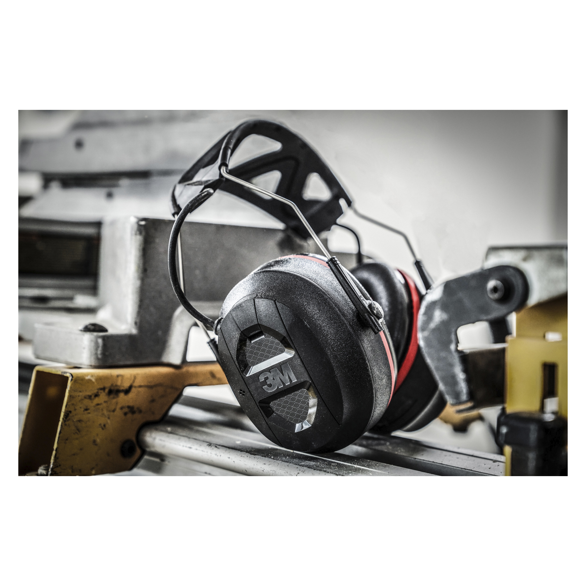 3M øreklokker med Bluetooth Pro-Protect henger fra en metallmaskinkomponent i et industrielt arbeidsområde.