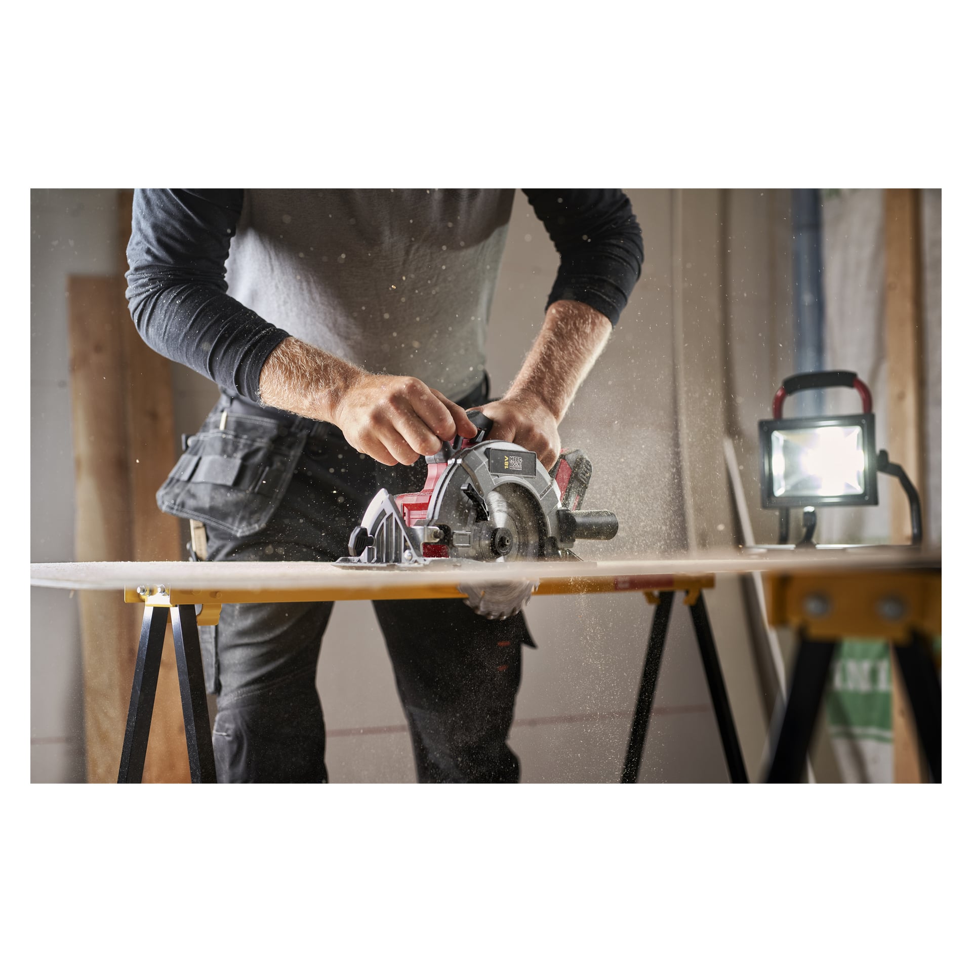 Joku leikkaa puulaudan työpöydälle Meec Tools Multiseries Starter -setillä, sahapuru lentää kirkkaassa valaistuksessa.