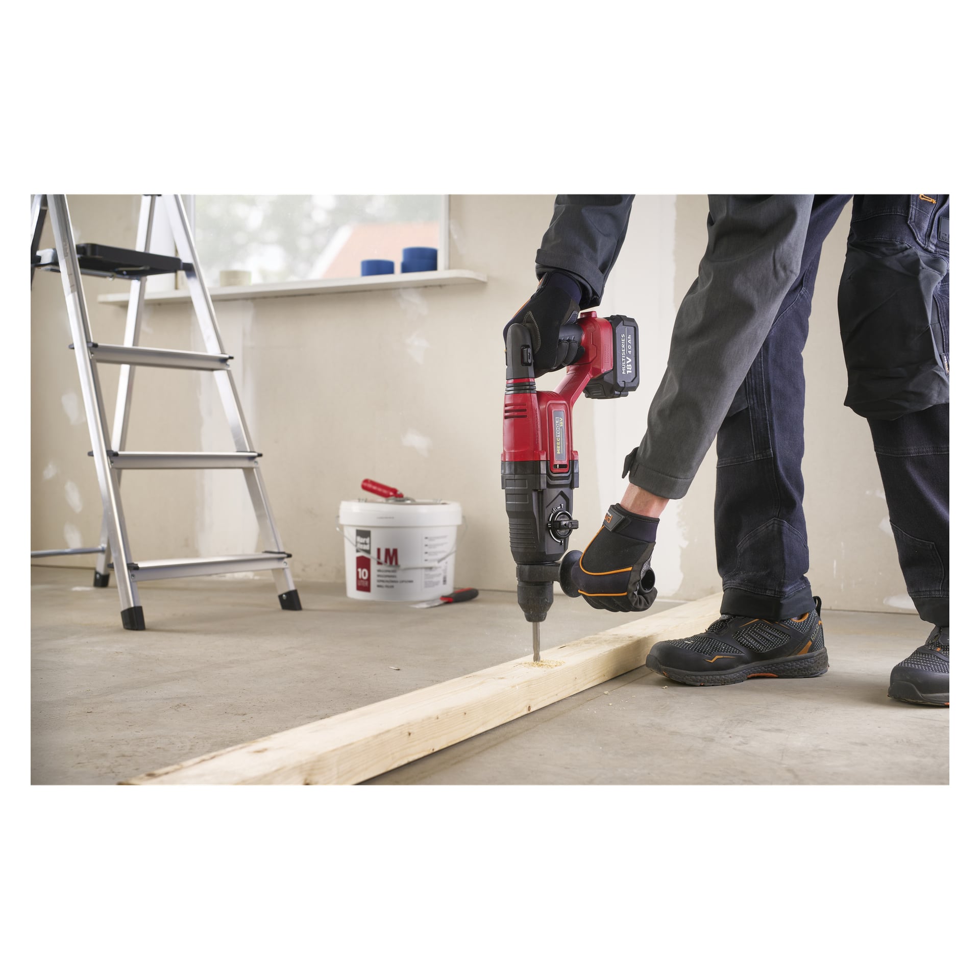 Osoba w rękawiczkach i butach wierci drewnianą belkę za pomocą Meec Tools HD-18V HOME 500; drabinę i wiadro z farbą w pobliżu.
