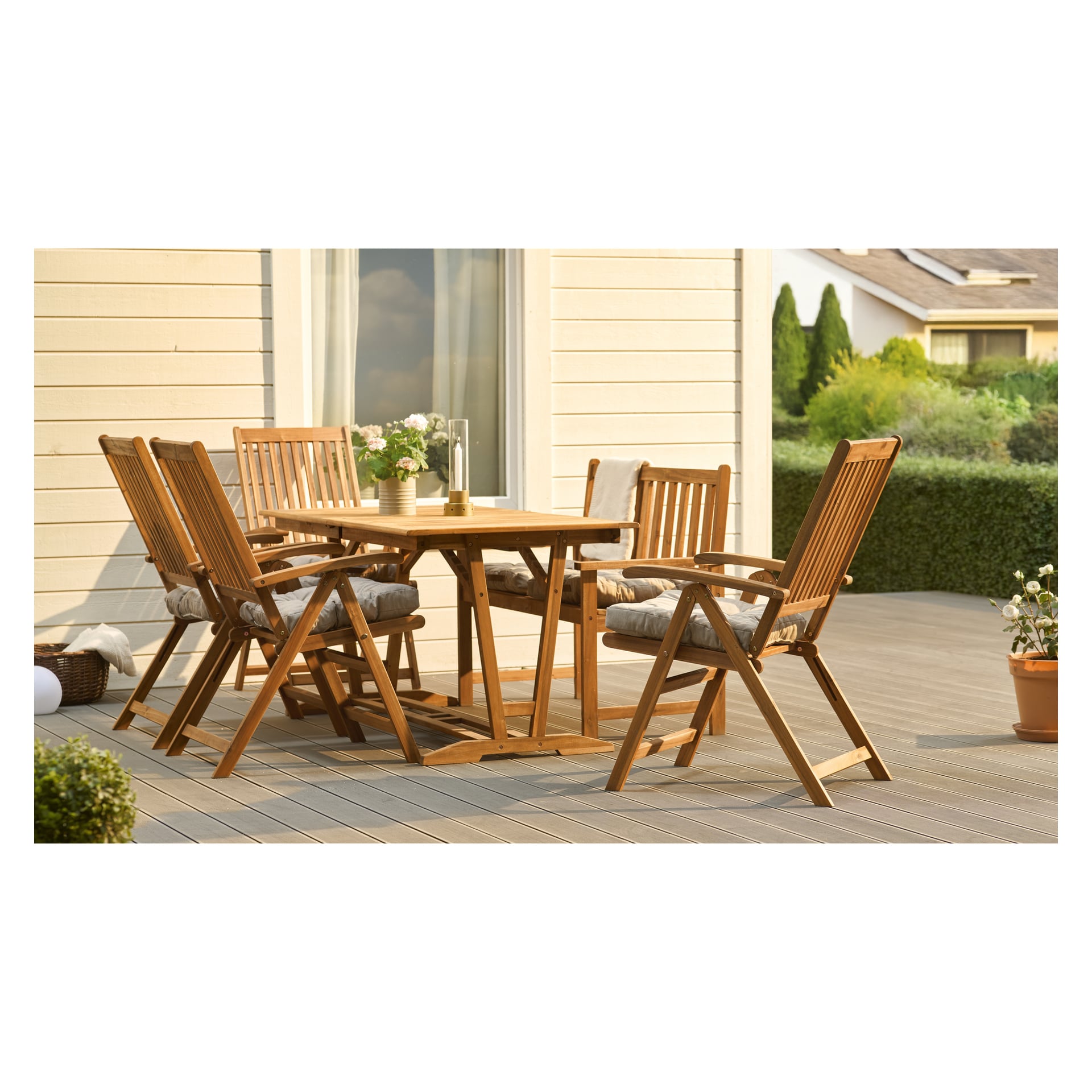 Et EKVIP sammenleggbart spisesett med seks justerbare stoler og et bord står på en terrasse, dekorert med blomster, planter og puter.