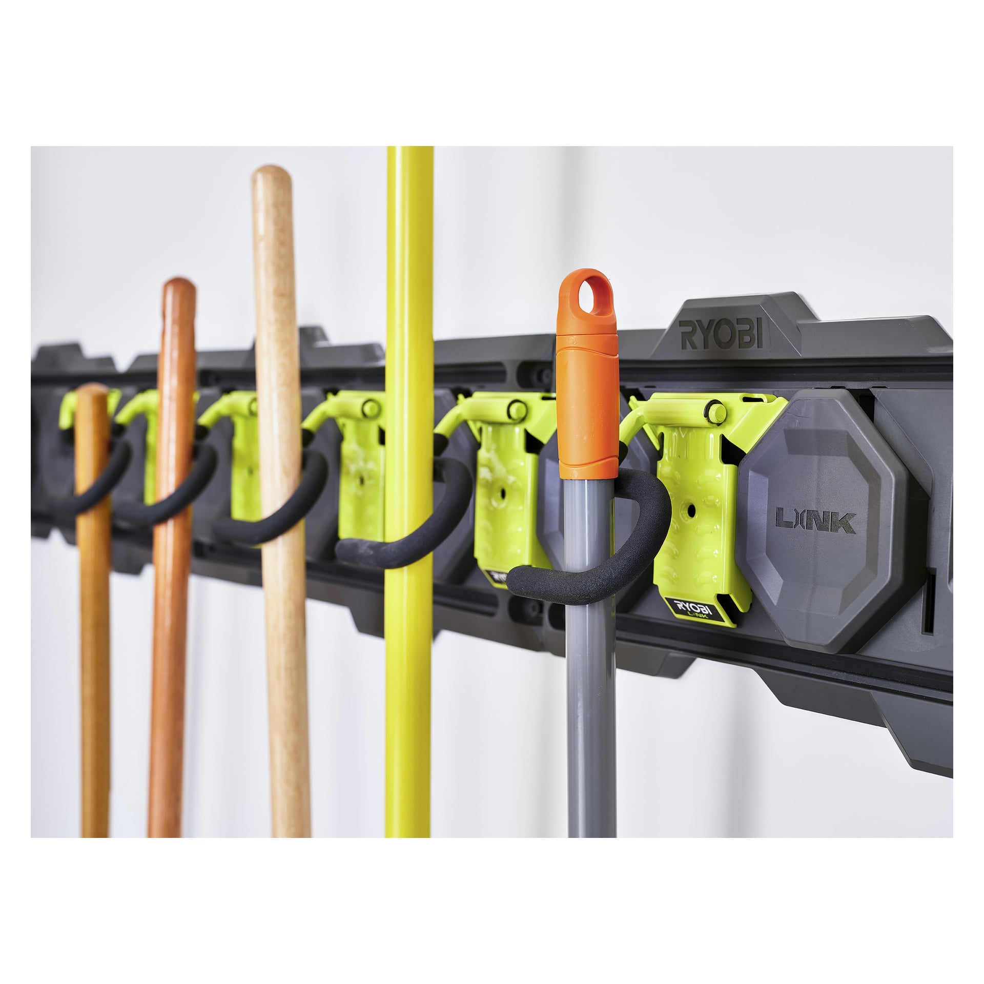 En Ryobi LINK RSLW802 verktygskrok fäster flera trä- och metallträdgårdsredskap vertikalt med fyra gula och svarta klämmor.