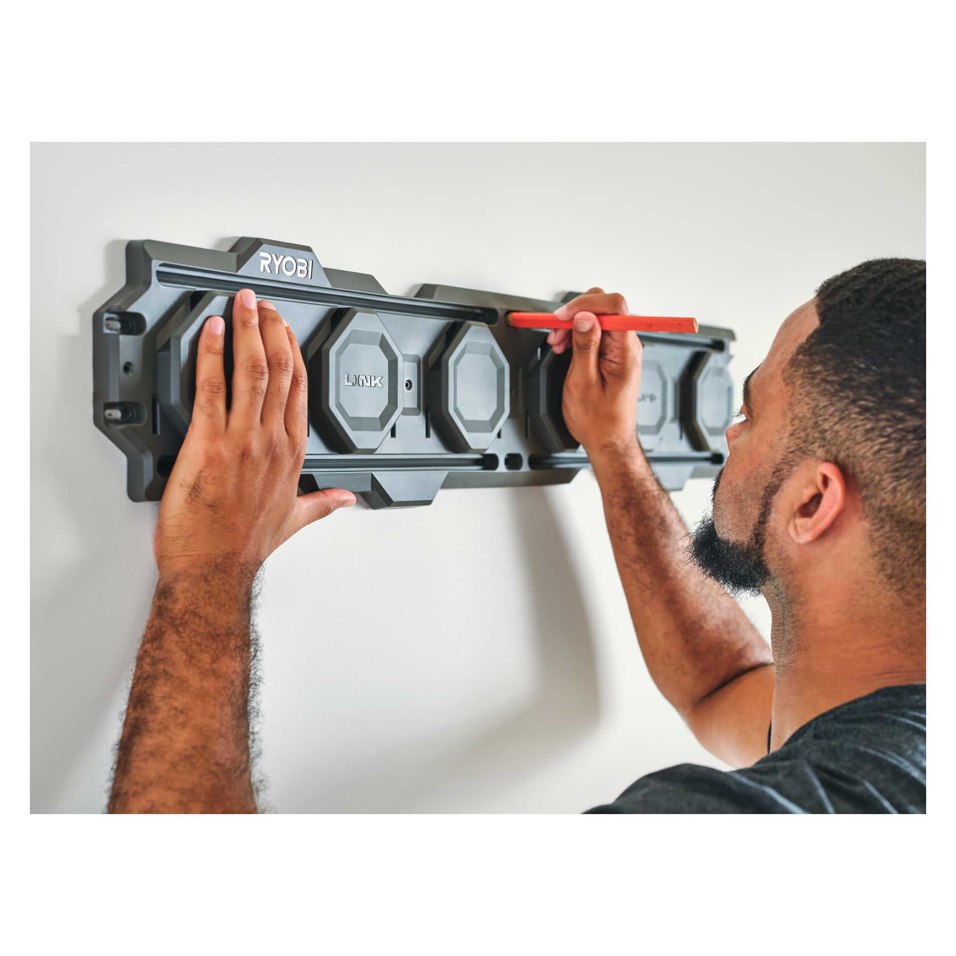 En person använder en röd penna för att markera en fläck på väggen medan man håller i en Ryobi Wall Rails LINK RSL2WR-2 2-pack med båda händerna.