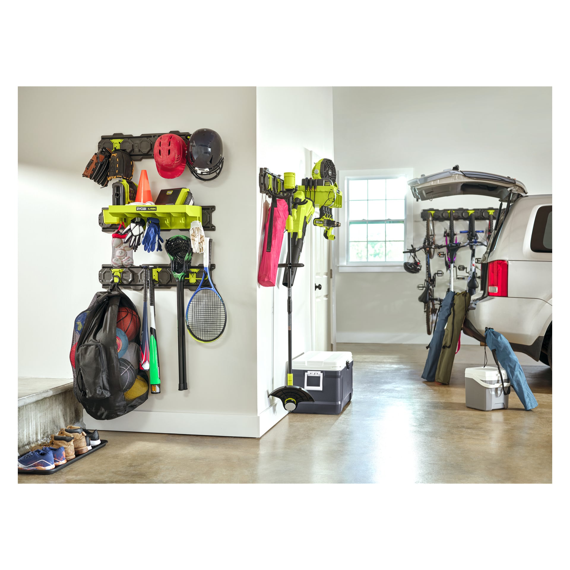 Ett snyggt garage med Ryobi LINK-rälser som förvarar hjälmar, verktyg och utrustning. Bilens bagageutrymme öppet nära kylväskor, stolar; Solljuset skiner in.