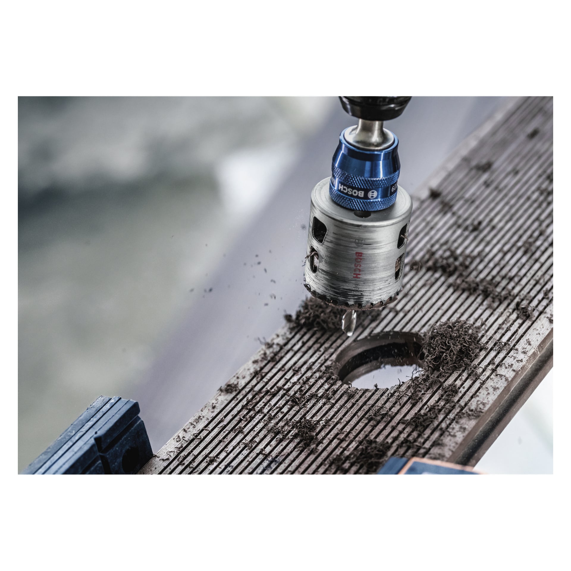 Bosch Pro Hole Saw BIM Power Change sopii poraan, koska se poraa reiän puuhun; Puunlastuja ja sininen puristin näkyvät.