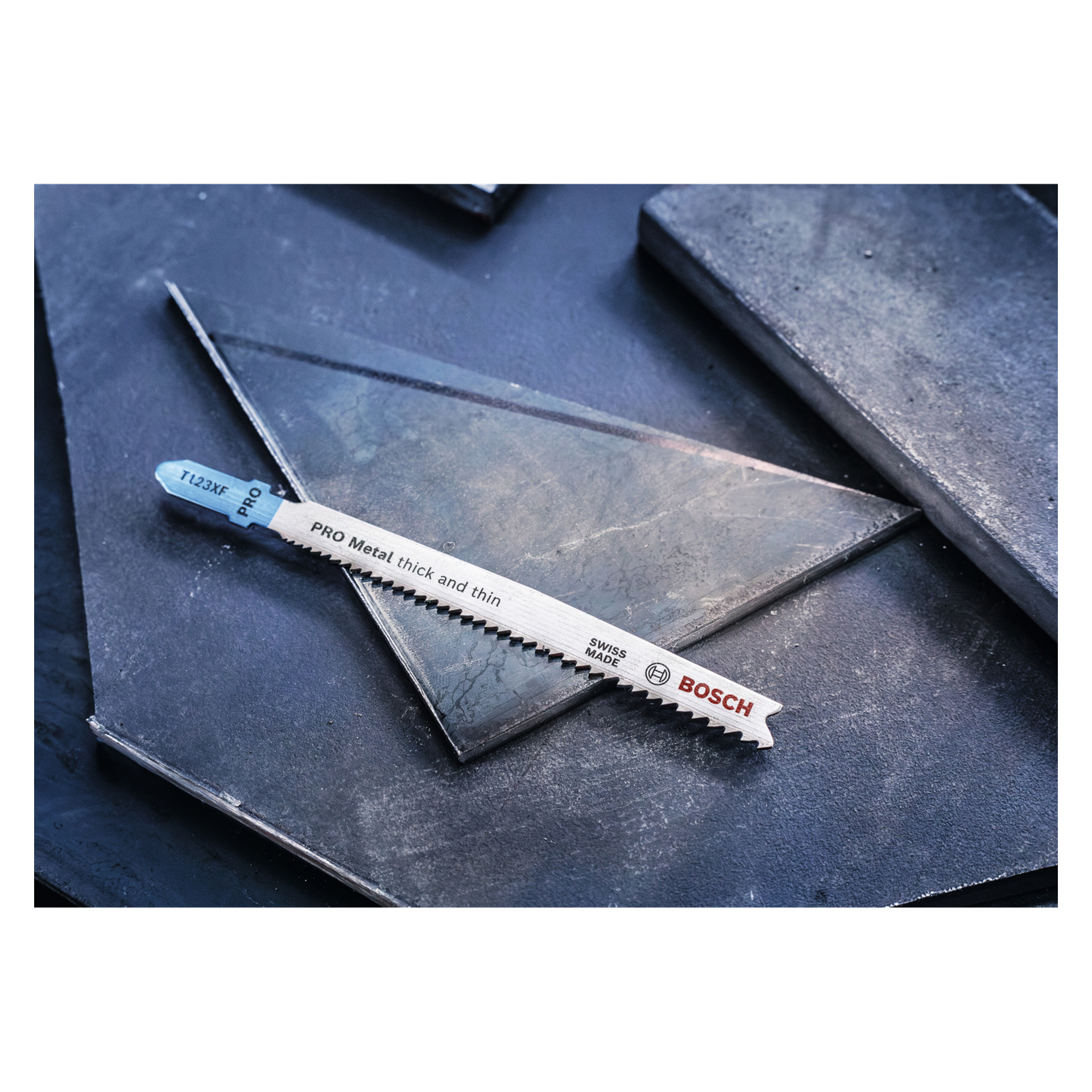 Ett Bosch Pro Jigsaw-blad T123XF PRO Metal (2-pack), märkt "Swiss Made", ligger diagonalt på en triangulär metallplatta bland mörka metaller.