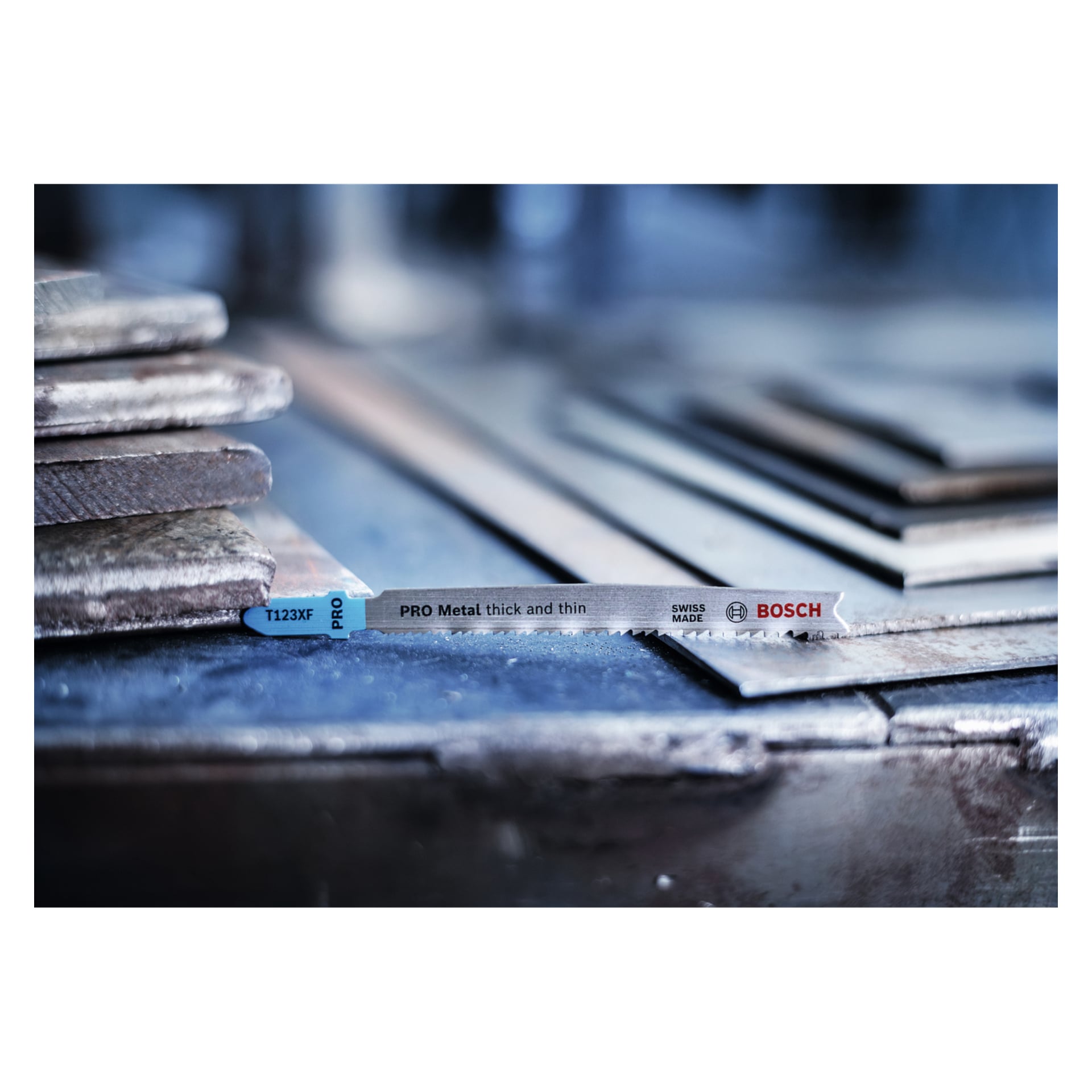 En Bosch Pro Jigsaw T123XF PRO Metal 2-pack för tjock och tunn metall vilar på staplade metallplåtar i en industriverkstad.