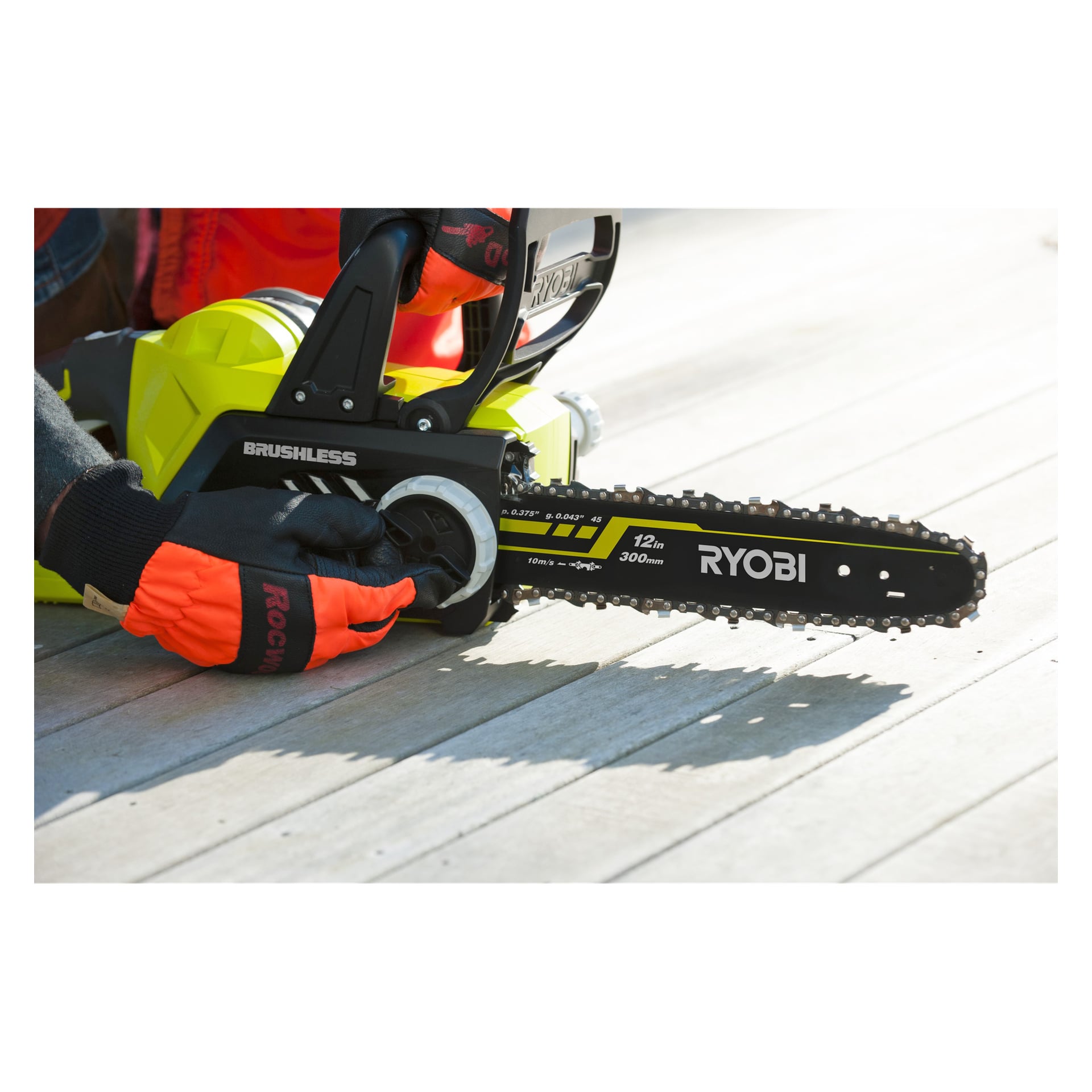 En person med oransje hansker vrir på spenningsknappen på en Ryobi One+ batteridrevet motorsag merket "RCS1830-150F," som står på en treflate.