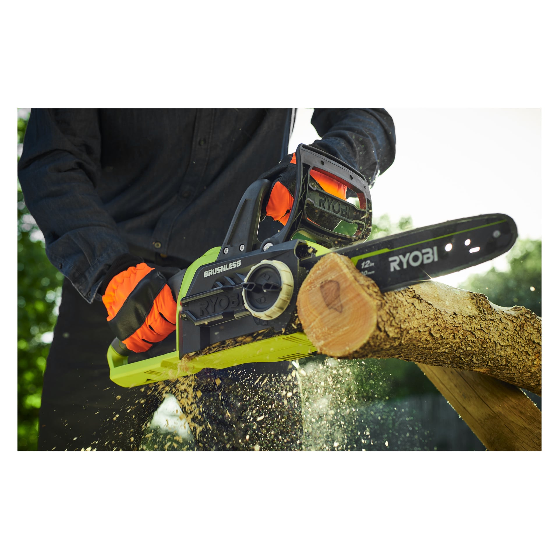 En person med oransje hansker og mørk skjorte betjener en Ryobi One+ batteridrevet motorsag merket "RCS1830-150F" for å kutte gjennom en tregren, med trefliser som flyr.