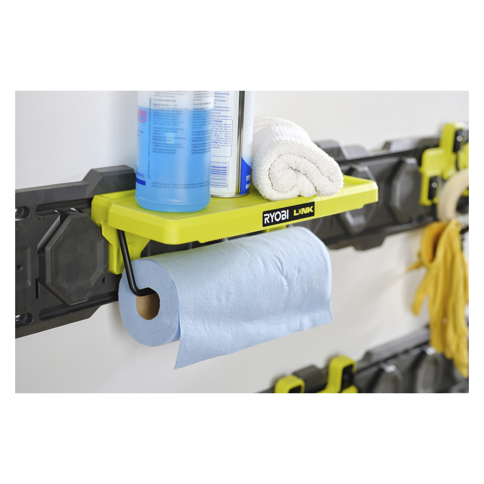 En Ryobi LINK RSLW403 hylla innehåller en blå sprayflaska, en rullad vit handduk och blå pappershanddukar på ett svart och gult räckesystem.