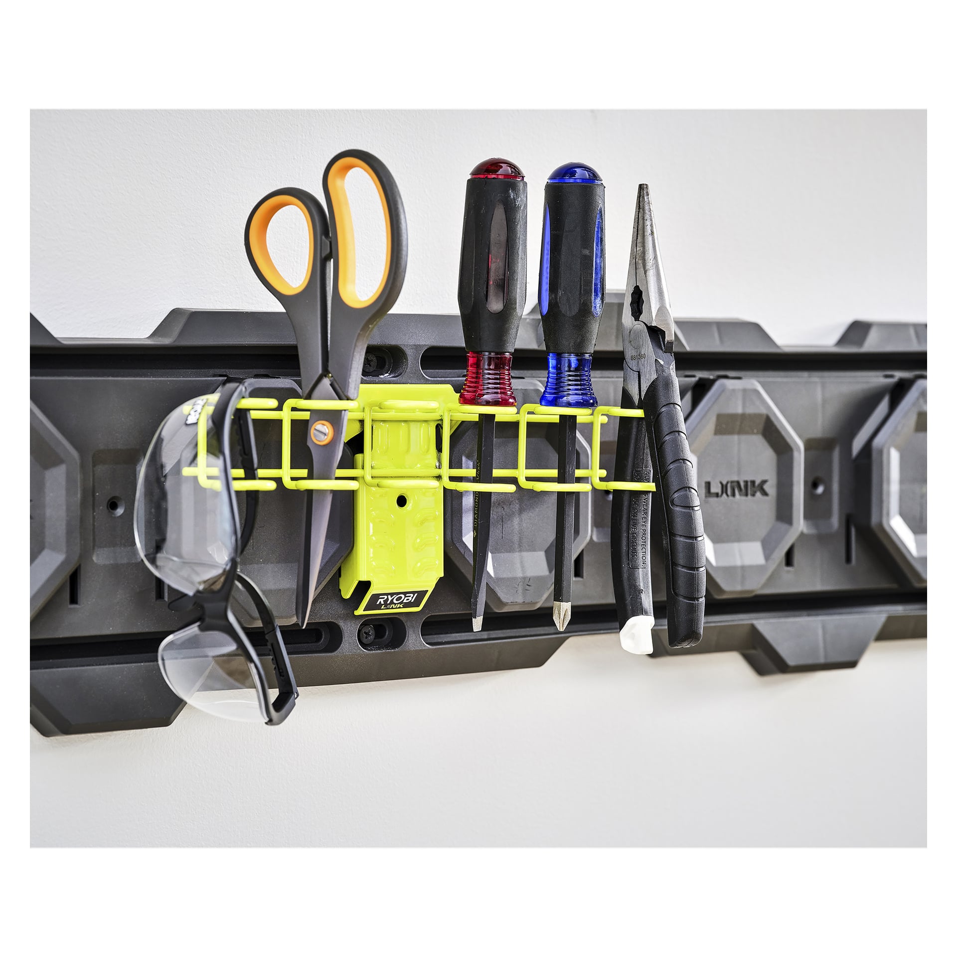 Veggmontert Ryobi LINK RSLW807 holder saks, to skrutrekkere, tang, sikkerhetsbriller og en gul verktøyholder.