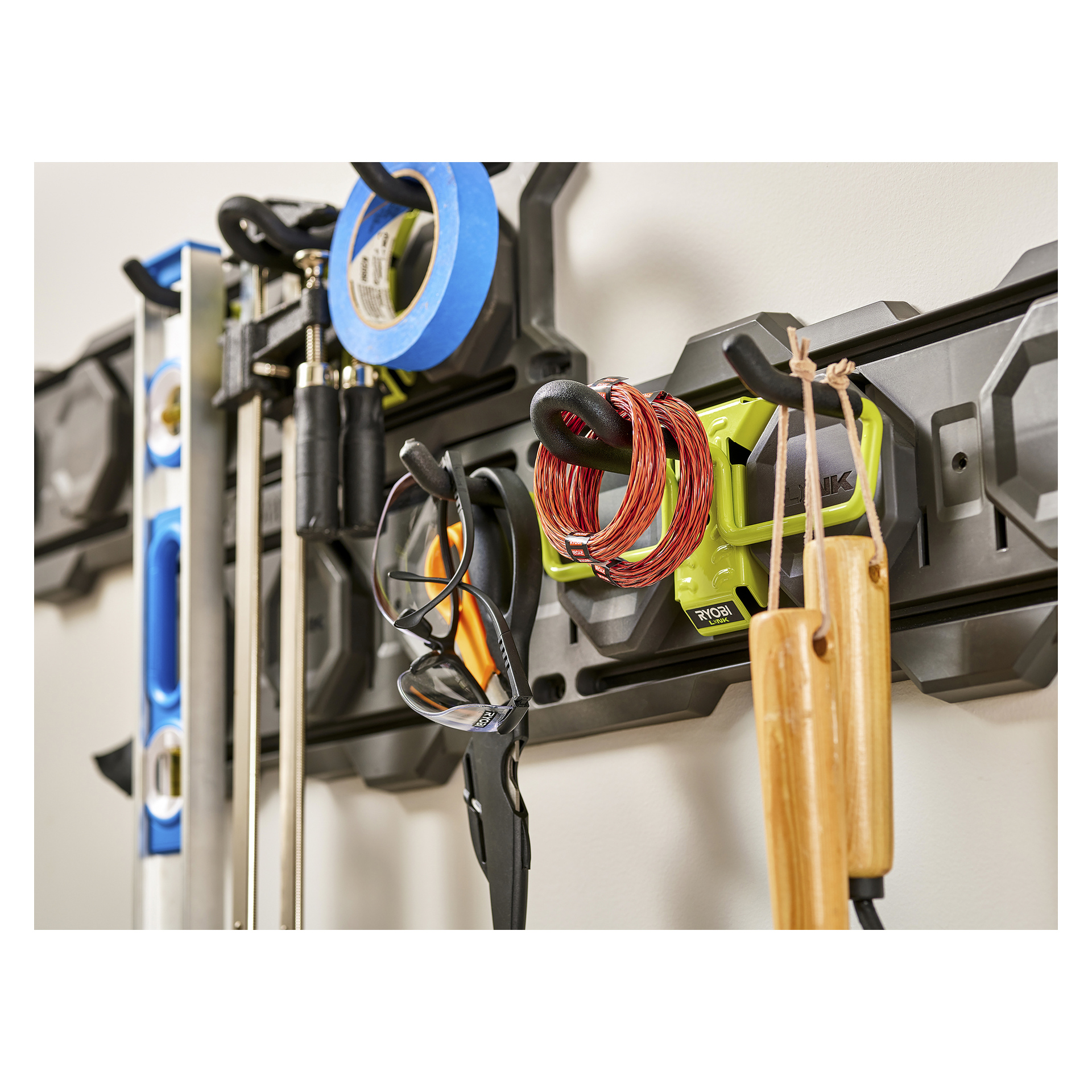 Närbild på en Ryobi LINK RSLW806 krok uppsatt på väggen, organiserad med vattenpass, tejp, skyddsglasögon, sladdar och nunchaku.