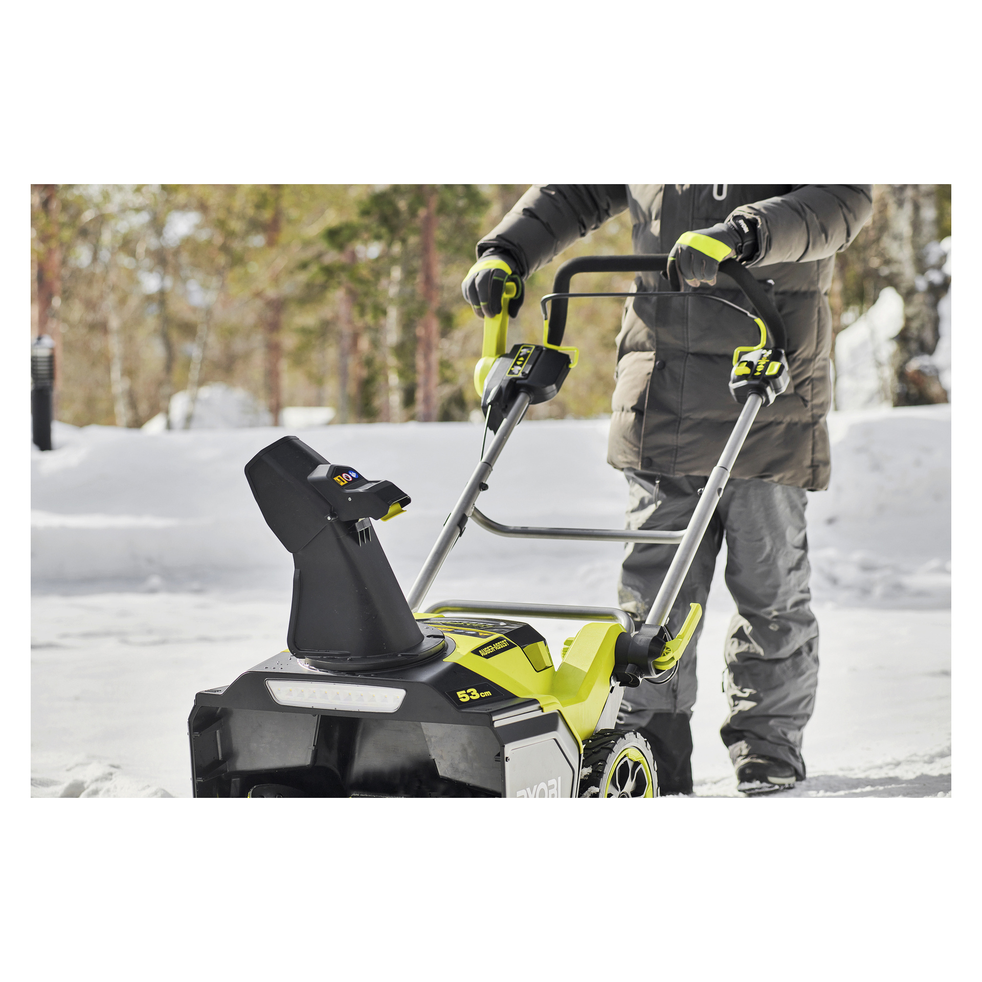 Klädd i vinterkläder kör man Ryobi Max Power snöslunga RY36STX53B-160 och röjer snö nära träd utomhus.