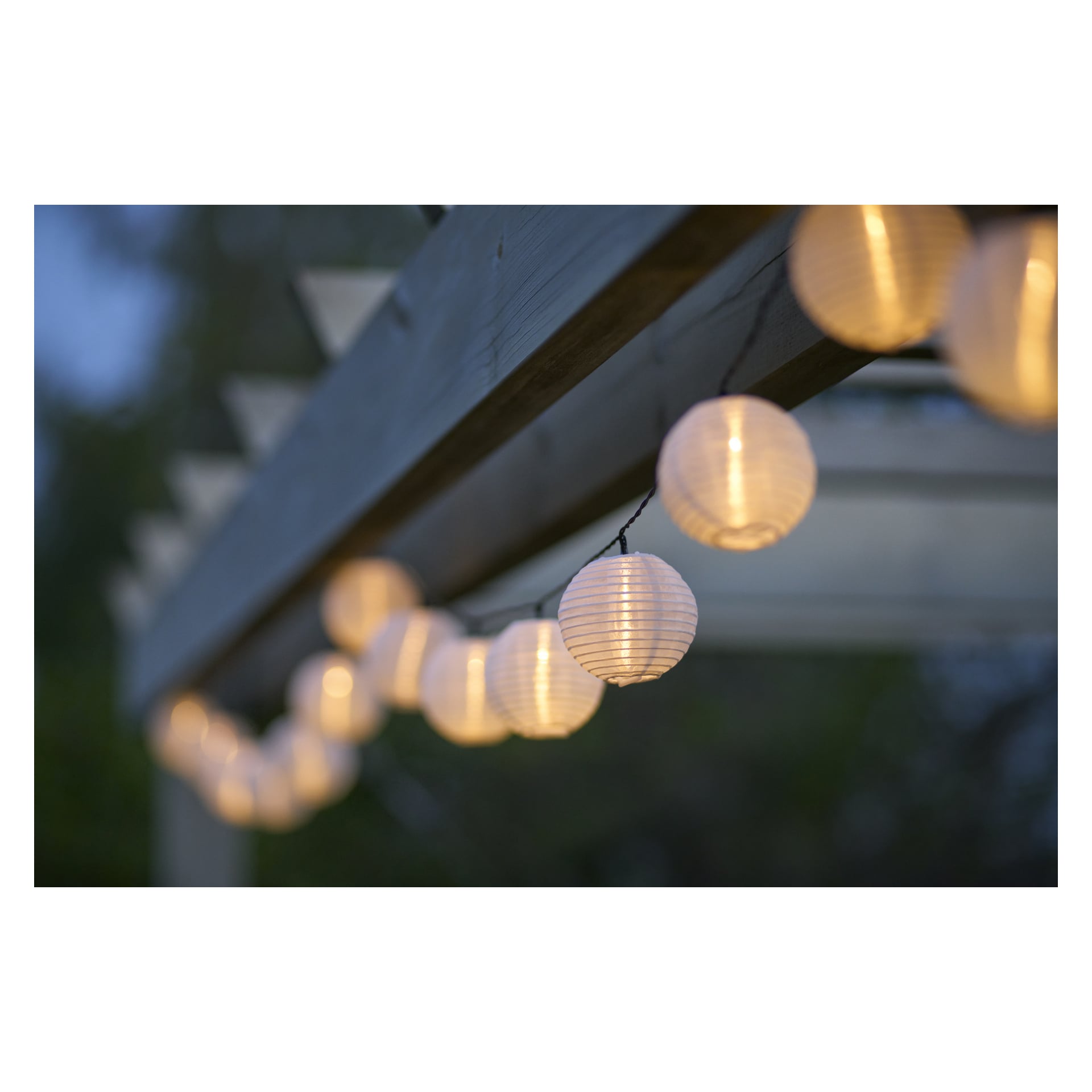 Solcellslampor med LED-ljus från Anslut hänger på en träpergola och kastar ett varmt sken mot mjuk grönska och en skymt himmel.