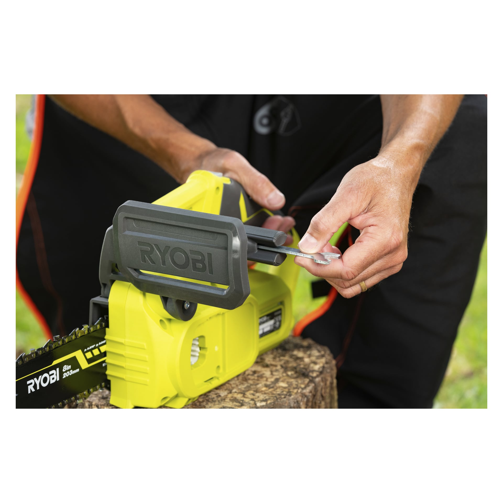 Hender bruker en skiftenøkkel til å sette sammen en Ryobi One+ batterimotorsag (RY18CS20A-125) på en trestubbe; Motorsag er delvis bygget.