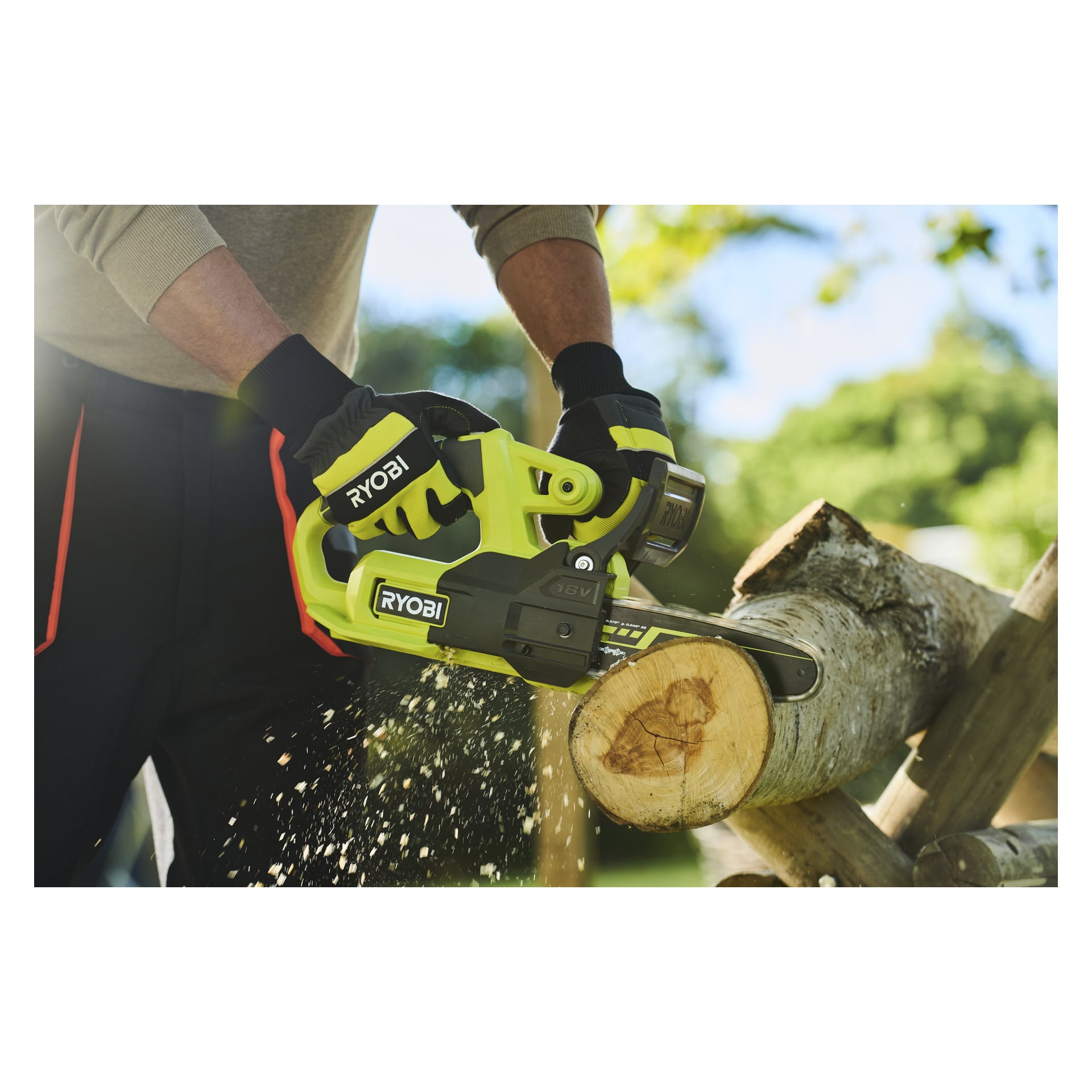 Hanskekledde hender betjener en Ryobi One+ batterimotorsag, kutter en tykk gren og sprer flis ute på en solrik dag.