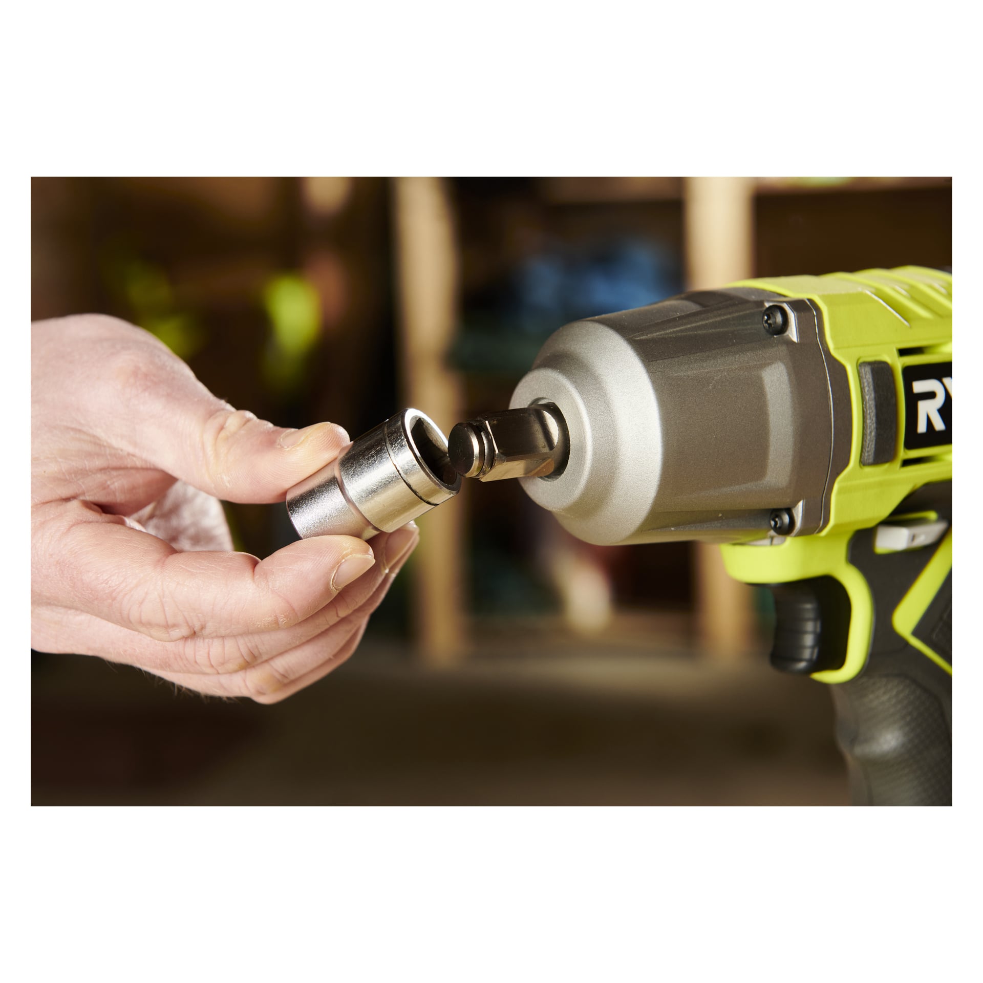 En hand fäster en metallhylsa på huvudet på en Ryobi One+ slagskruvsats RIW18-1C20SA3 i en verkstadmiljö.