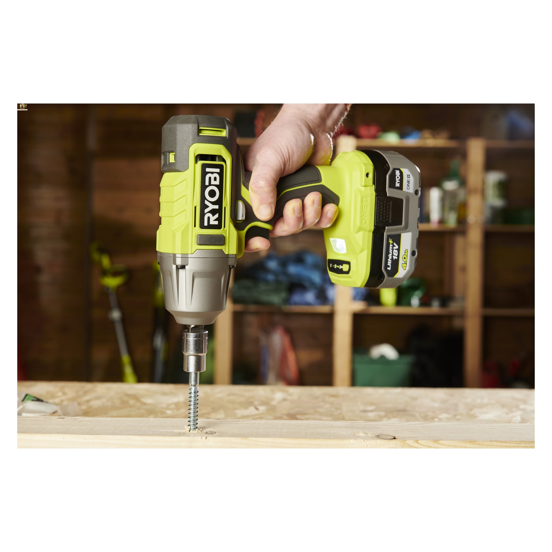 Någon använder ett Ryobi One+ slagnyckelkit RIW18-1C20SA3 för att fästa en stor skruv i trä; Verkstadshyllorna suddas ut bakom.