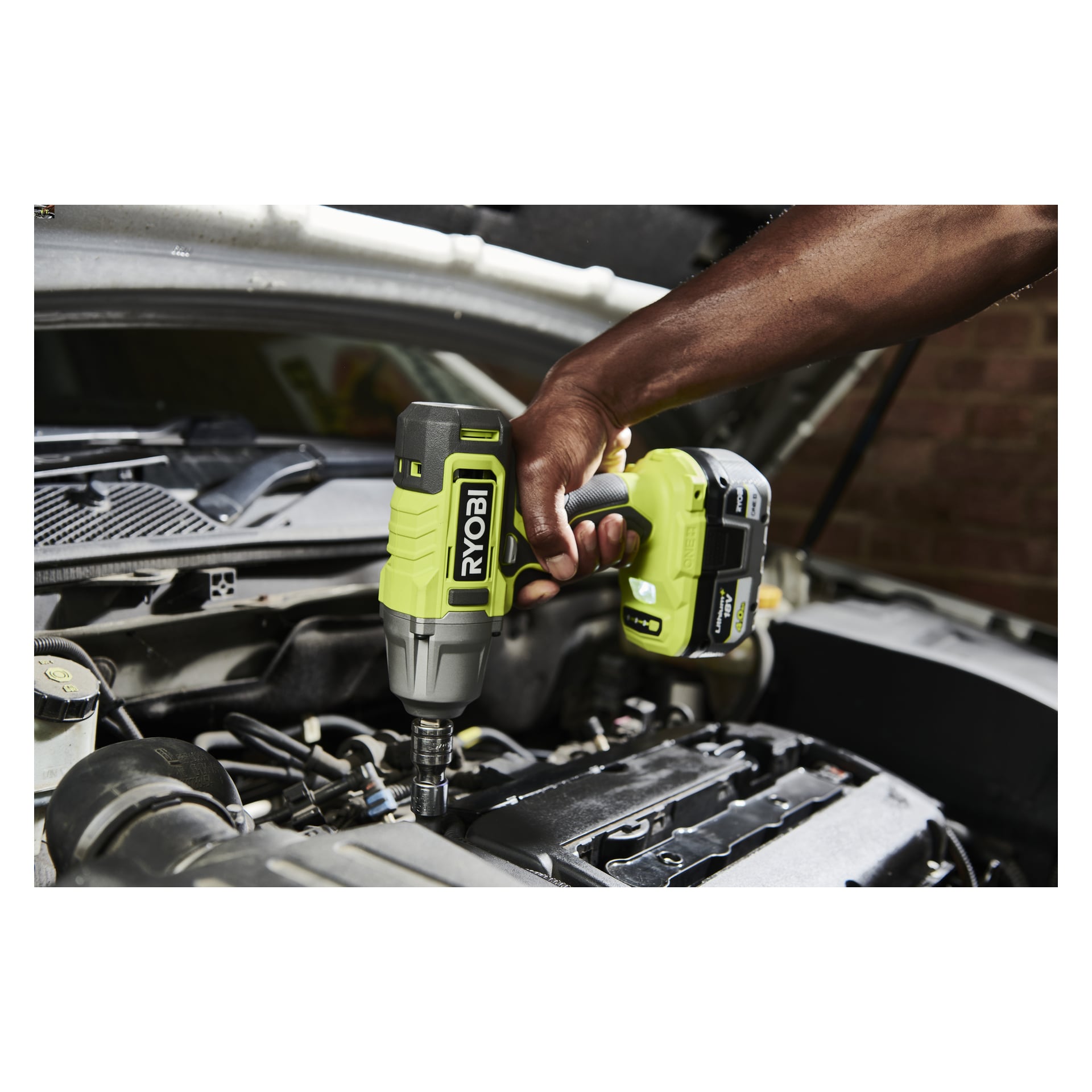 Noen bruker en Ryobi One+ Impact Wrench Kit RIW18-1C20SA3 over et åpent motorrom med panseret hevet.