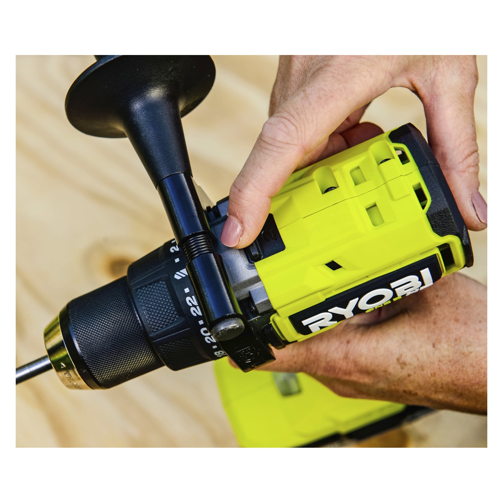 Man justerar inställningarna på en gul-svart Ryobi One+ HP borstlös skruvmejsel och tillbehörskit över en tunn träyta.