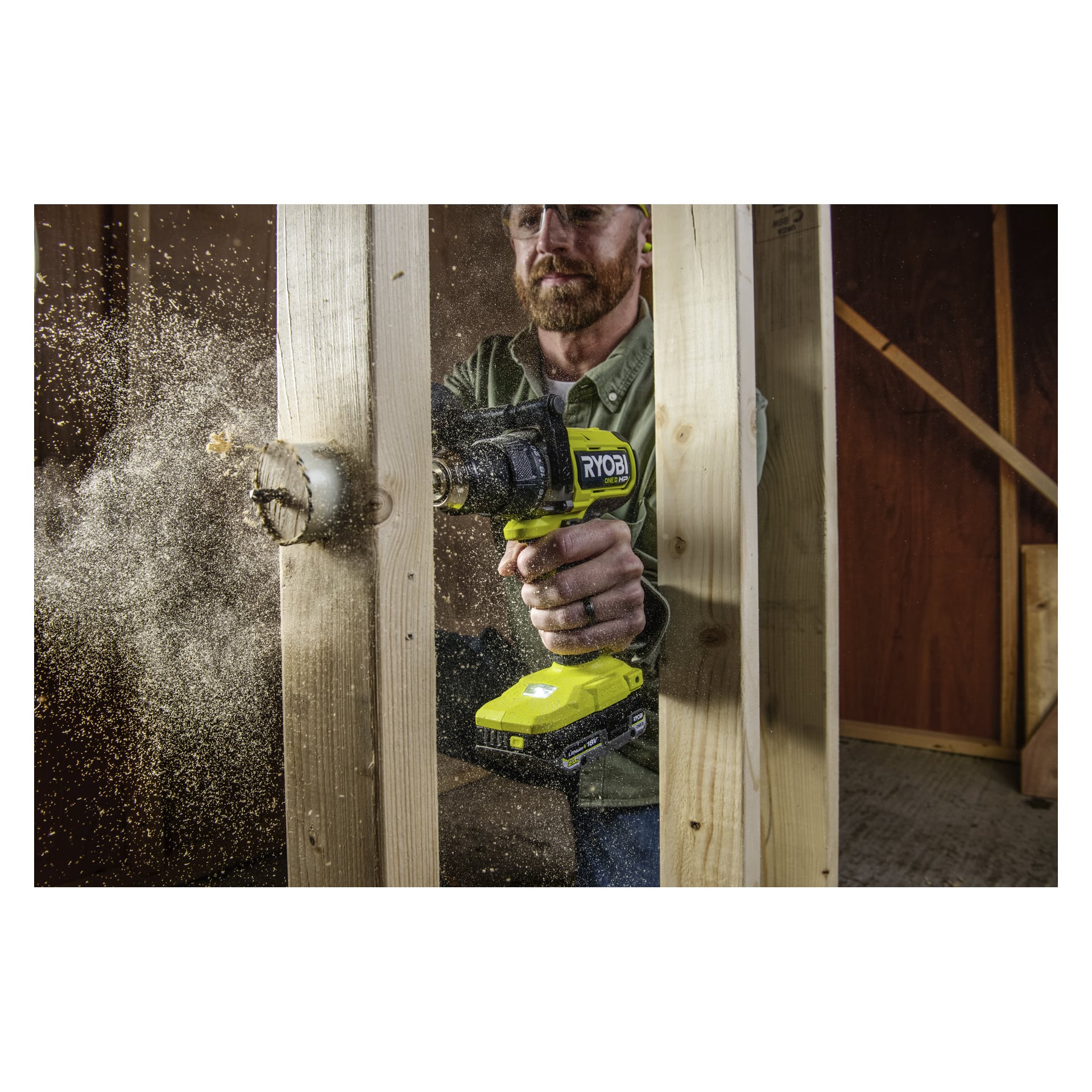 En person med skyddsglasögon borrar i en träregle med hjälp av Ryobi One+ HP Brushless-kit, sågspån sprids från borrpunkten.