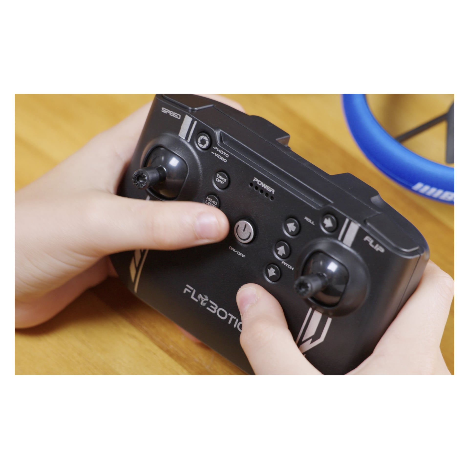Ręce korzystające z czarnego kontrolera Silverlit z joystickami do Bumper Drone Vision Wifi; Niebieski dron częściowo widoczny za nimi.