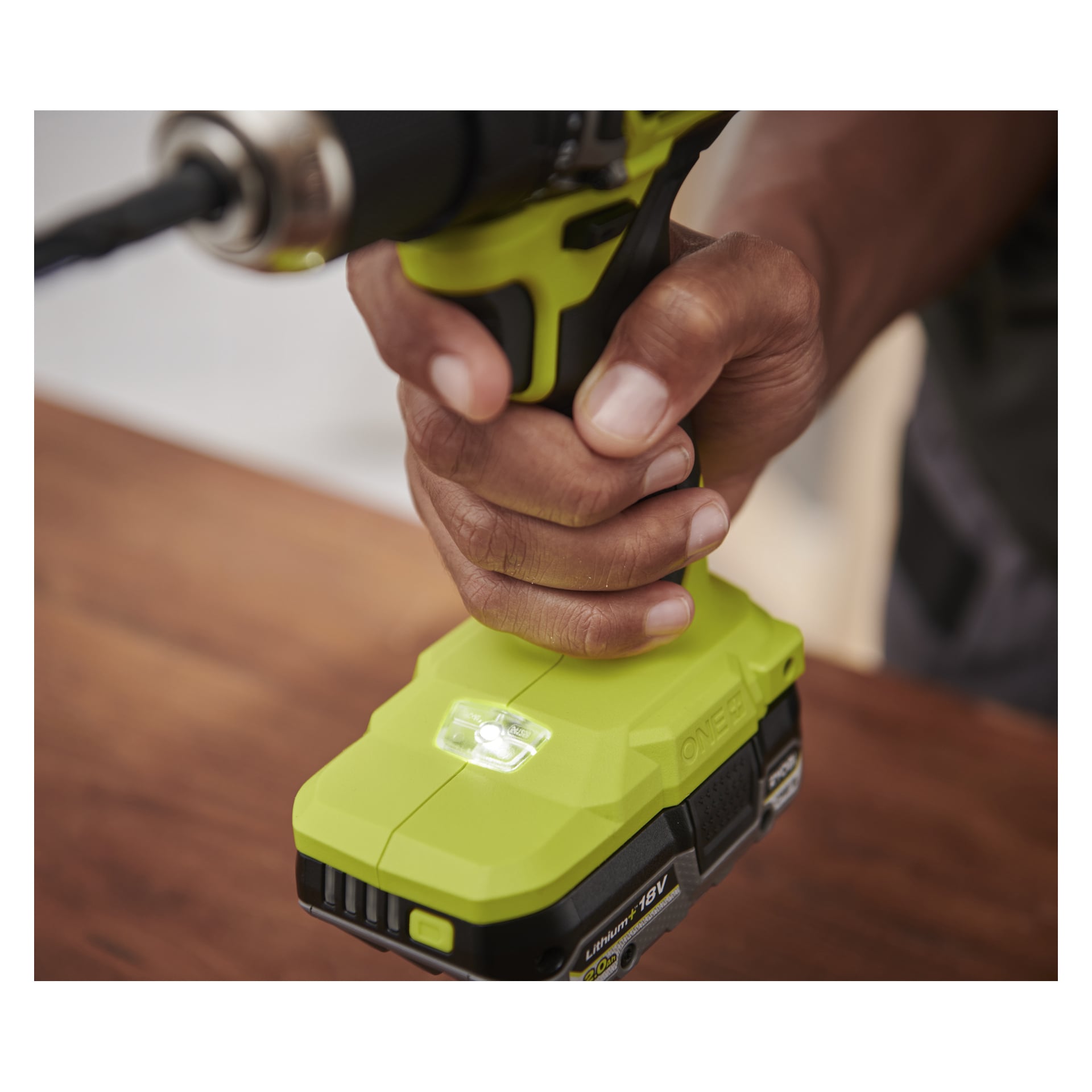 Jemand hält einen Ryobi One+ HP bürstenlosen Bohrer mit zwei Batterien, die auf Holz ruhen, was den Akku und das LED-Licht betont.