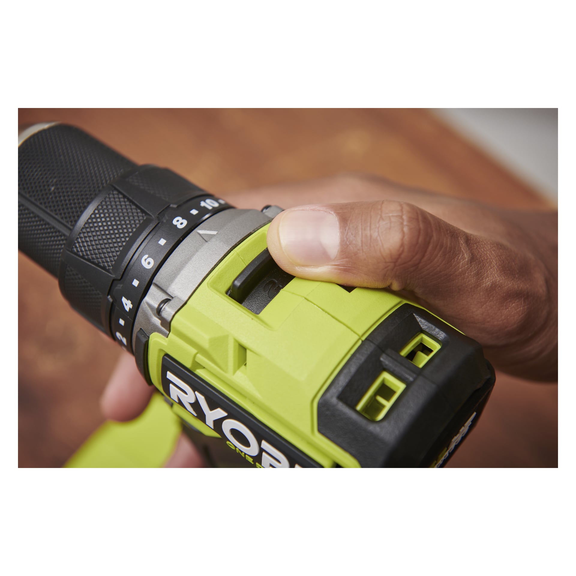 Eine Hand dreht den Knopf und den Schalter an einem grünen Ryobi One+ HP bürstenlosen Bohrschrauber mit zwei Batterien, der teilweise das Ryobi-Logo zeigt.